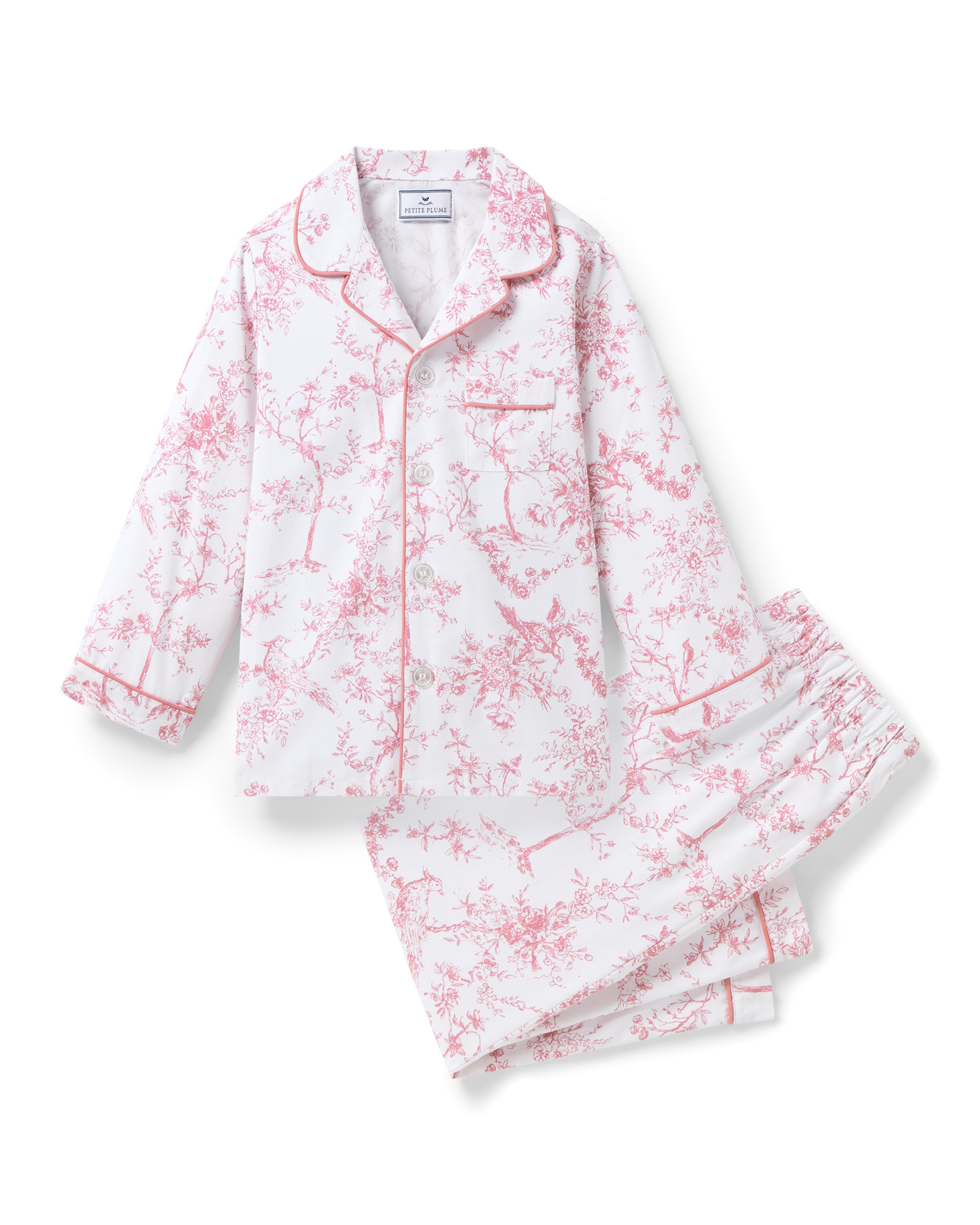 Experience botanical elegance with Petite Plumes Kids Twill Pajama Set in Pink Timeless Toile, adorned with floral patterns. Crafted from yarn-dyed cotton, it includes a long-sleeve button-up top with a chest pocket and matching pants, both featuring red piping for luxury sleepwear.