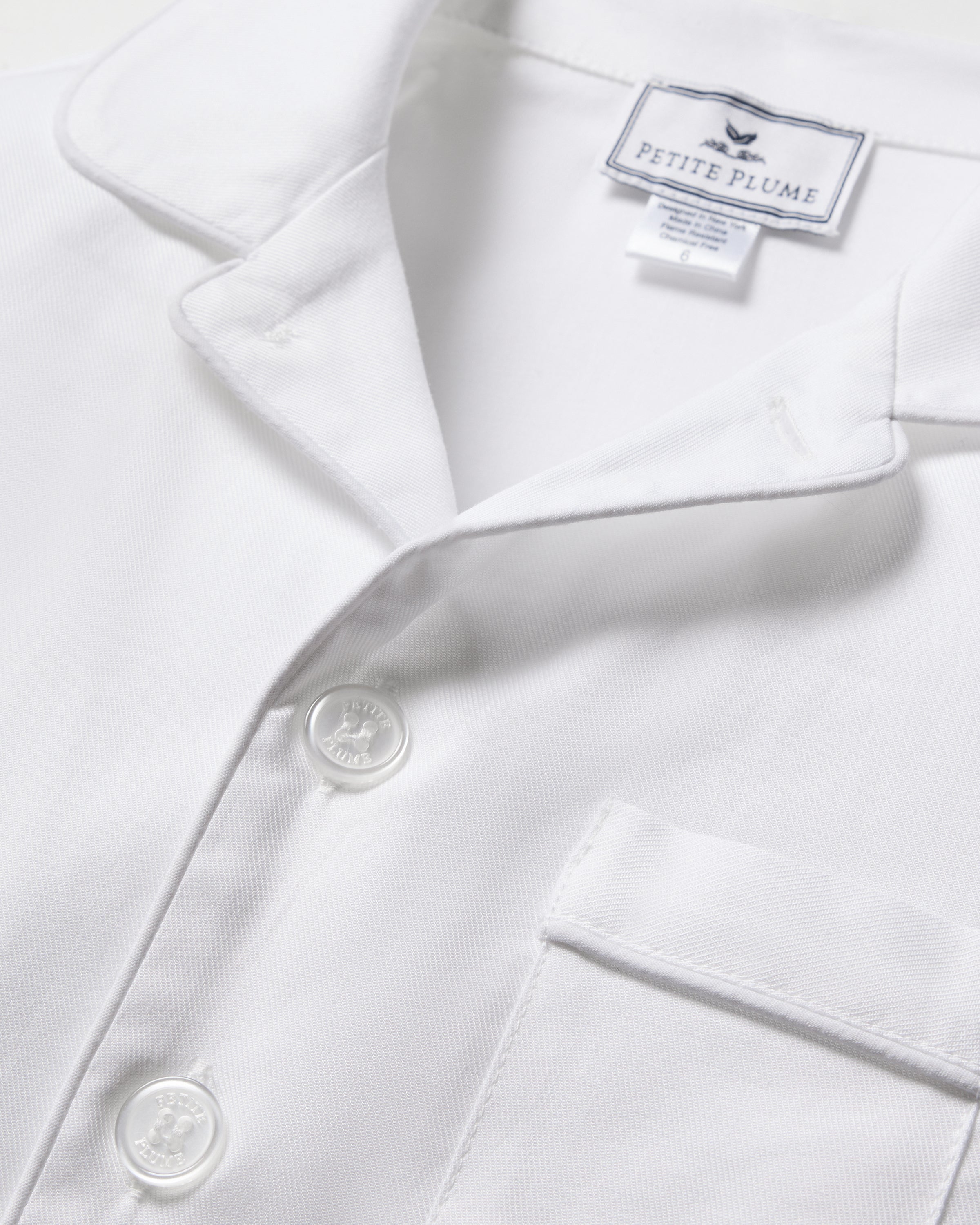 Close-up of the Kids Twill Pajama Set in White with White Piping by Petite Plume, featuring a smooth texture, soft collar, pocket on the front, and neatly aligned buttons. Perfectly curated for comfort and style in your nighttime routine.