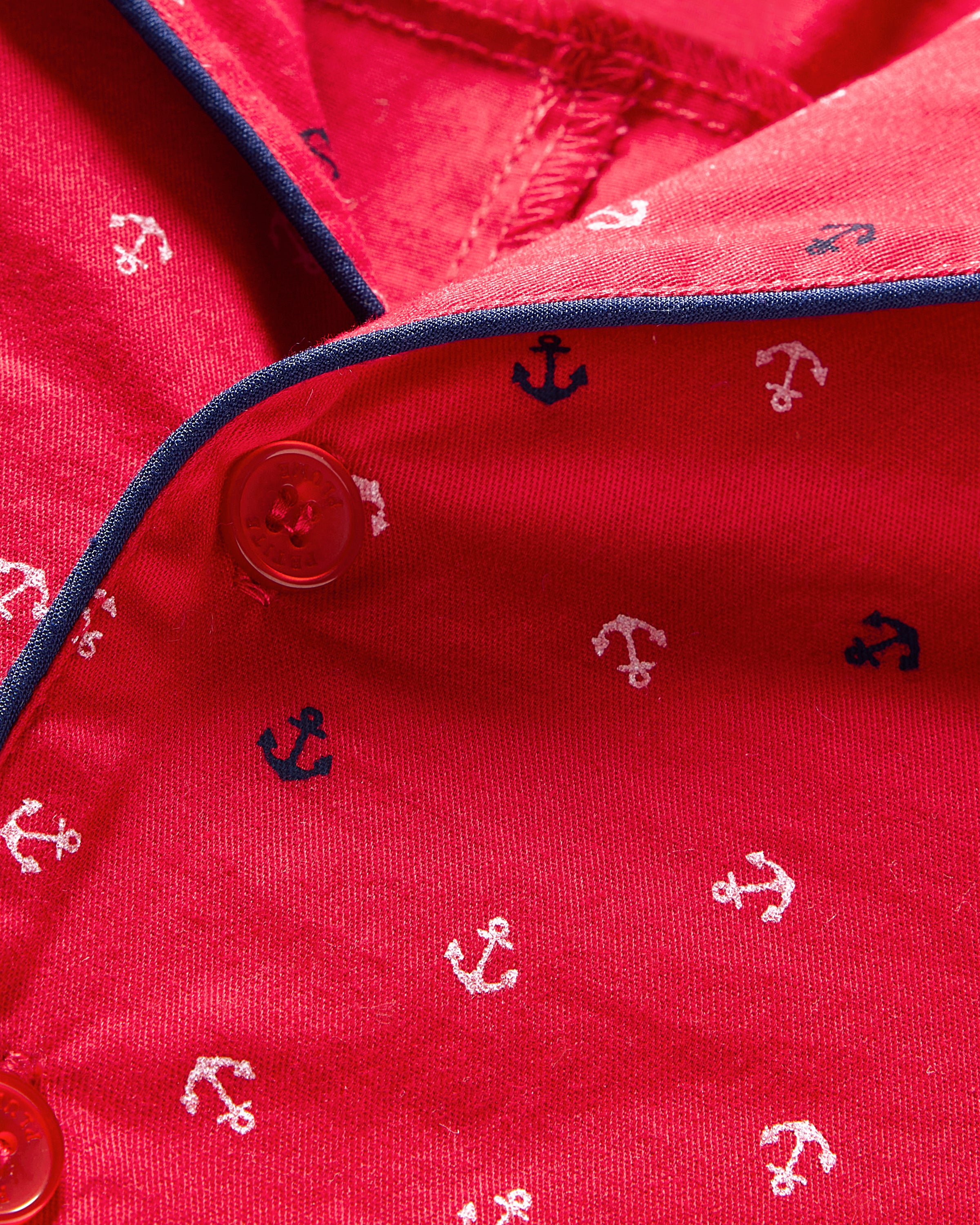 Close-up of Petite Plumes Babys Twill Summer Romper in Anchors Away, featuring red brushed twill with white and navy anchors, buttoned section, and navy piping outlining a nautical theme.