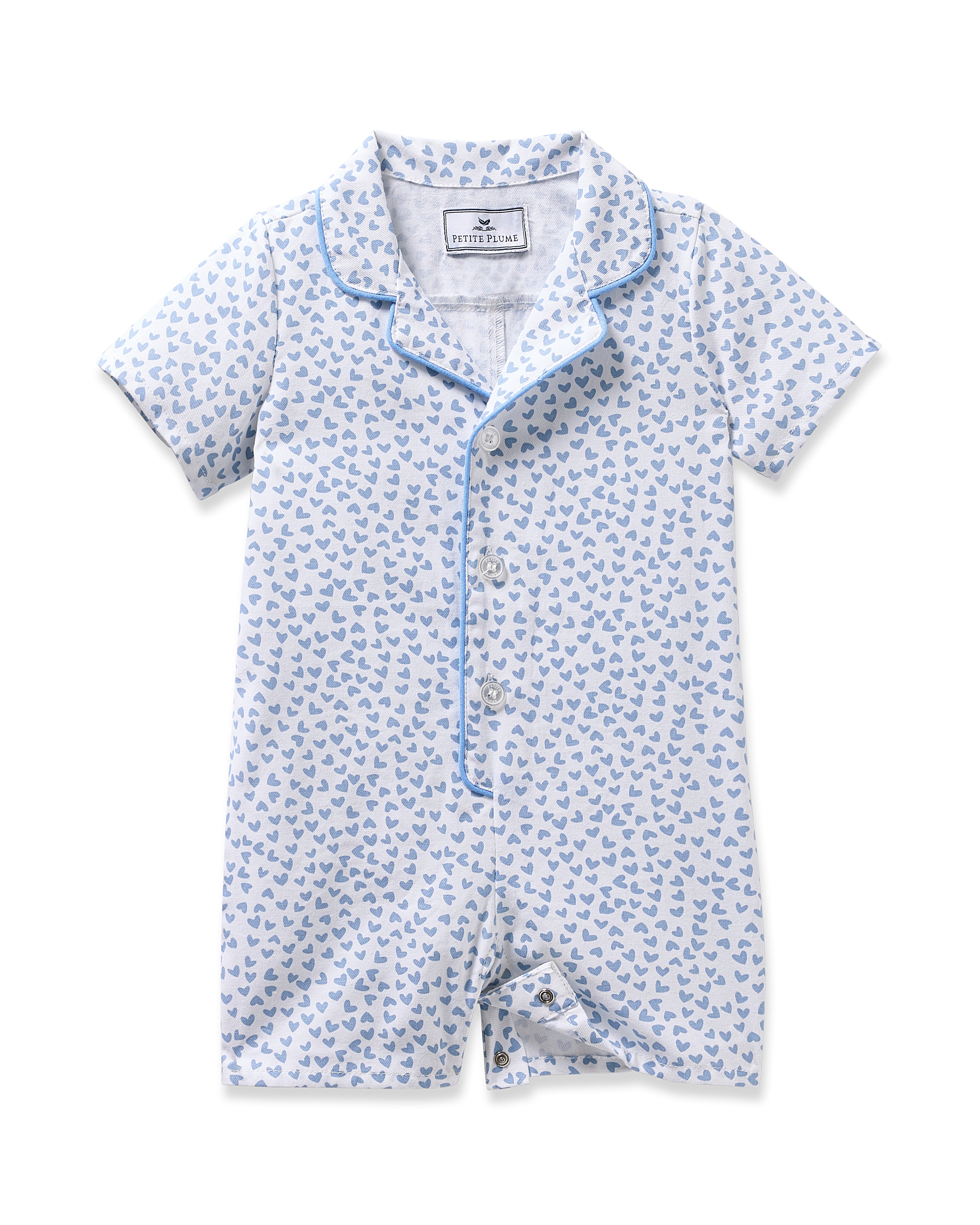 Petite Plumes Babys Twill Romper in Bluehearts is a light blue brushed twill romper adorned with small blue whales, featuring short sleeves, a collar, and a button-down front with blue piping along the edges.