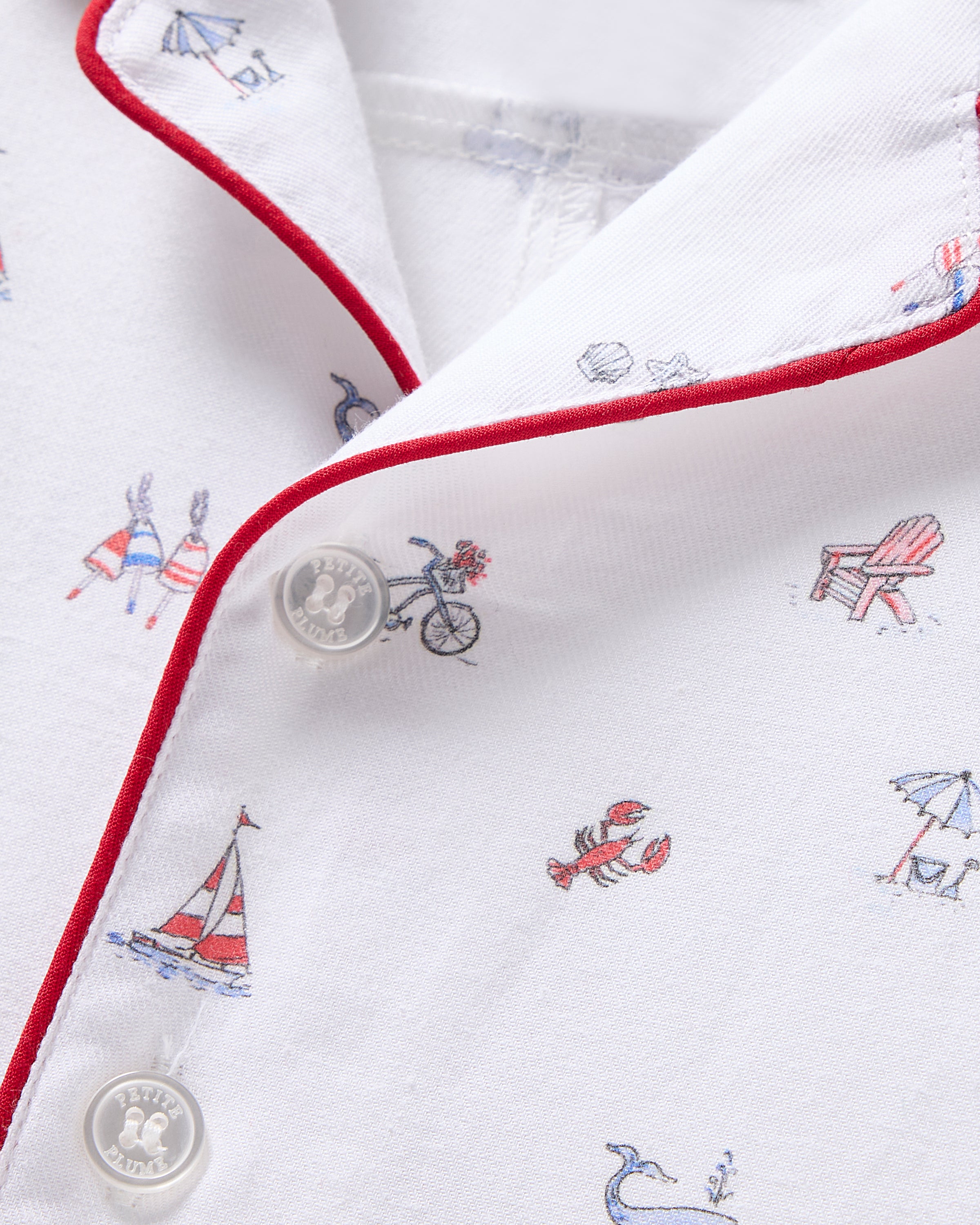 Close-up of Petite Plumes Babys Twill Summer Romper in Coastal Charms prints with bicycles, Adirondack chairs, sailboats, and lobsters. It features brushed twill fabric, red piping on the collar, and clear buttons.