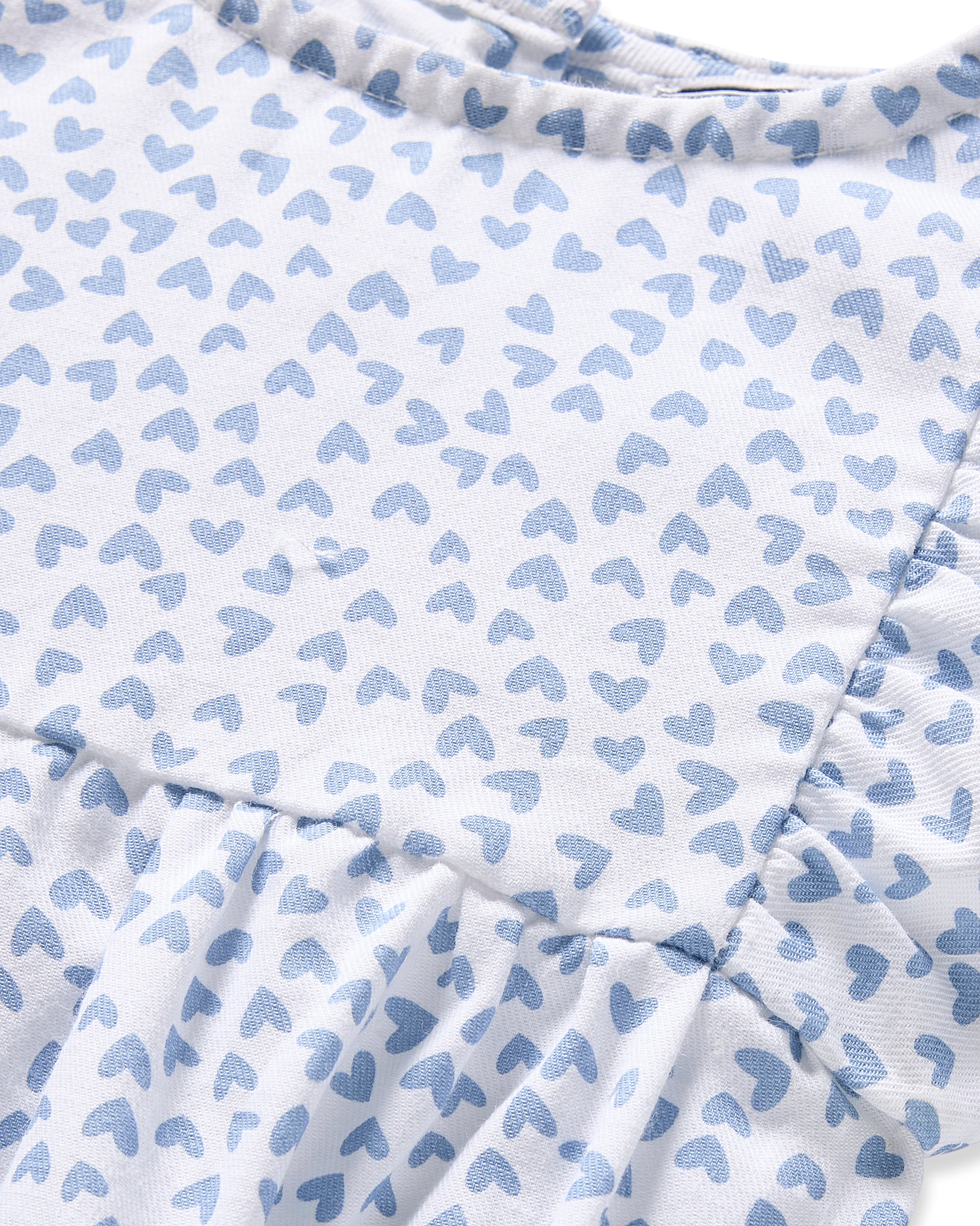 A close-up of Petite Plumes Babys Twill Ruffled Romper in Bluehearts on a white background showcases the romper crafted from flame retardant fiber with a gathered seam for a subtle ruffle, ideal for minimalist sleepwear.