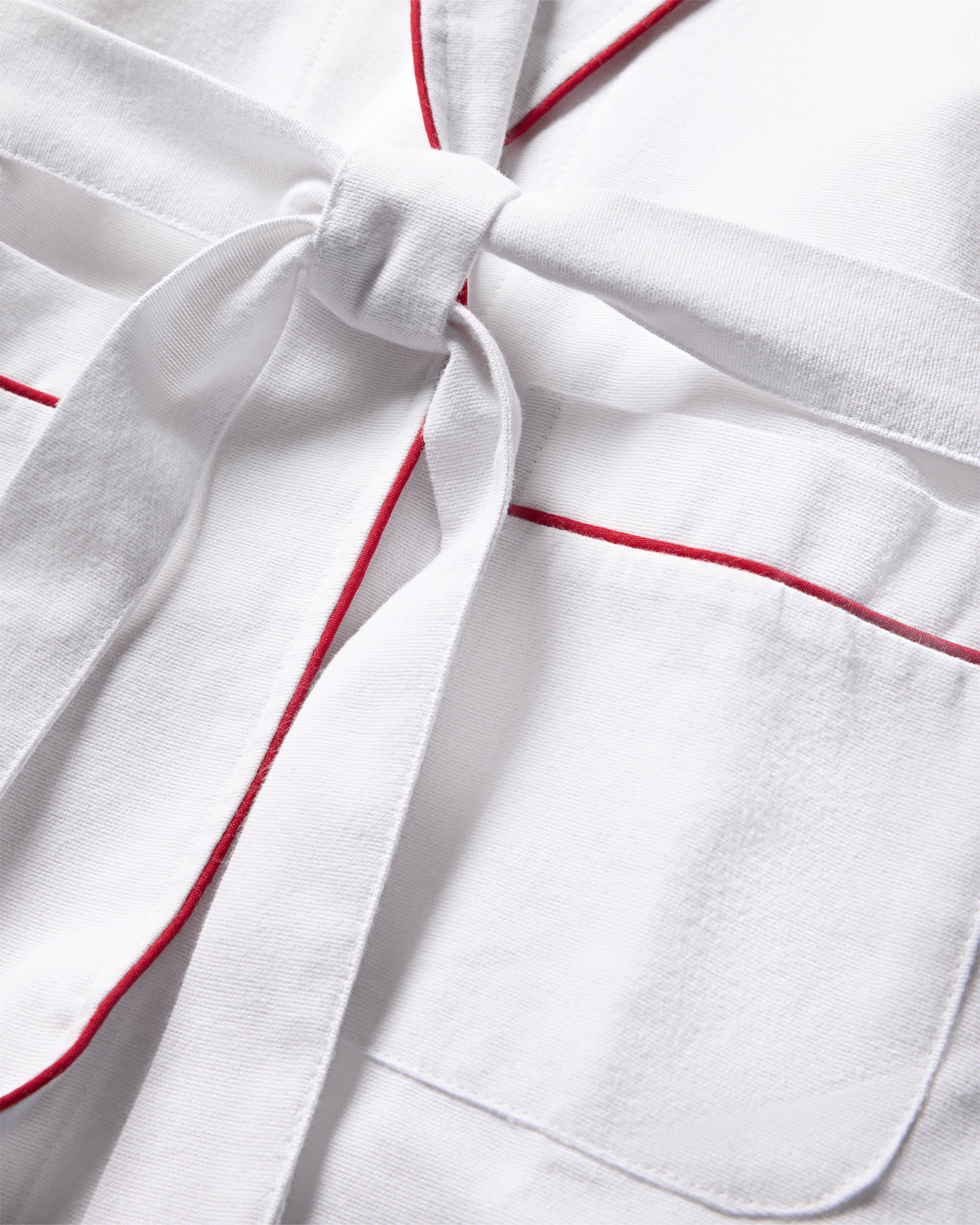 Close-up of Petite Plumes Kids Flannel Robe in White with Red Piping, featuring a fabric belt. Its perfect for childrens sleepwear, offering a soft and plush texture with flame-retardant safety.