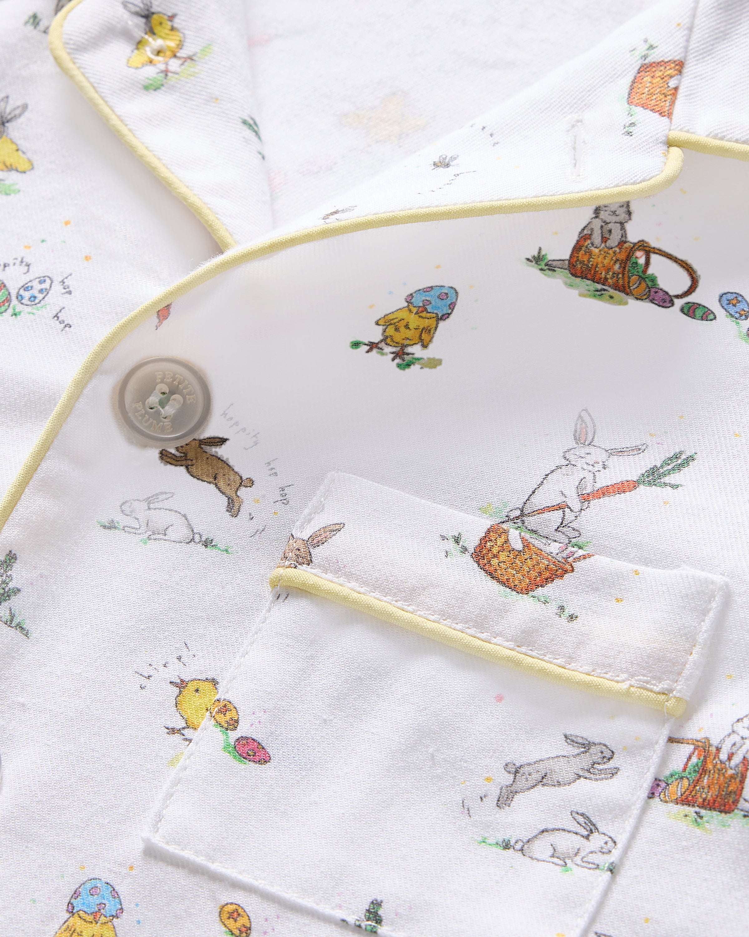 Close-up of the Kids Twill Short Set by Petite Plume in the Easter Frolic print, showcasing whimsical rabbits, birds, and mushrooms. Accented with thin yellow piping, it features a partially visible button and pocket for added charm.