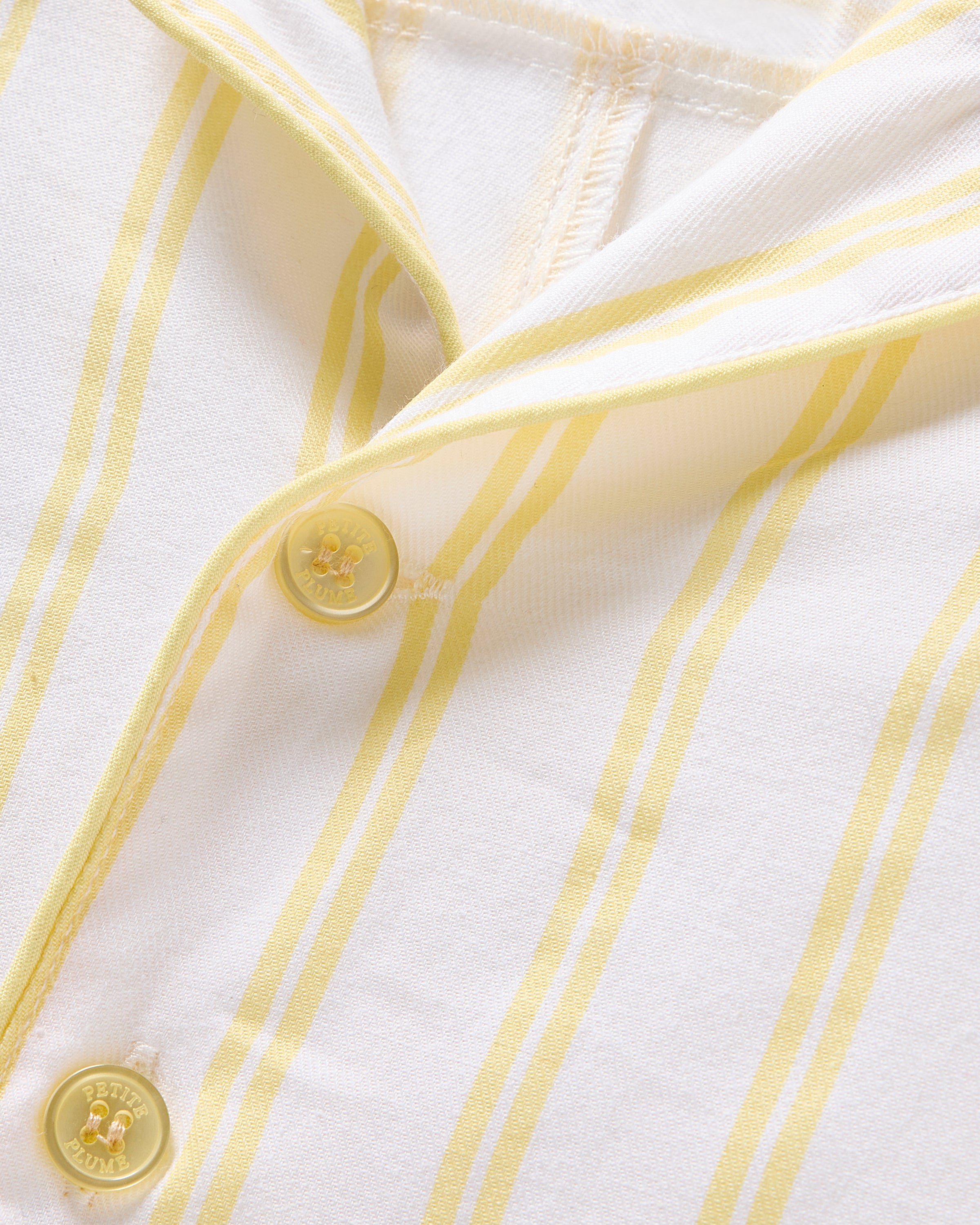 Close-up of the Kids Twill Short Sleeve Short Set in Sunny Stripe by Petite Plume shows a white cotton shirt with yellow stripes and two buttons. The soft fabric has a subtle texture, and the buttons have a small center design, perfect for cozy sleepwear.