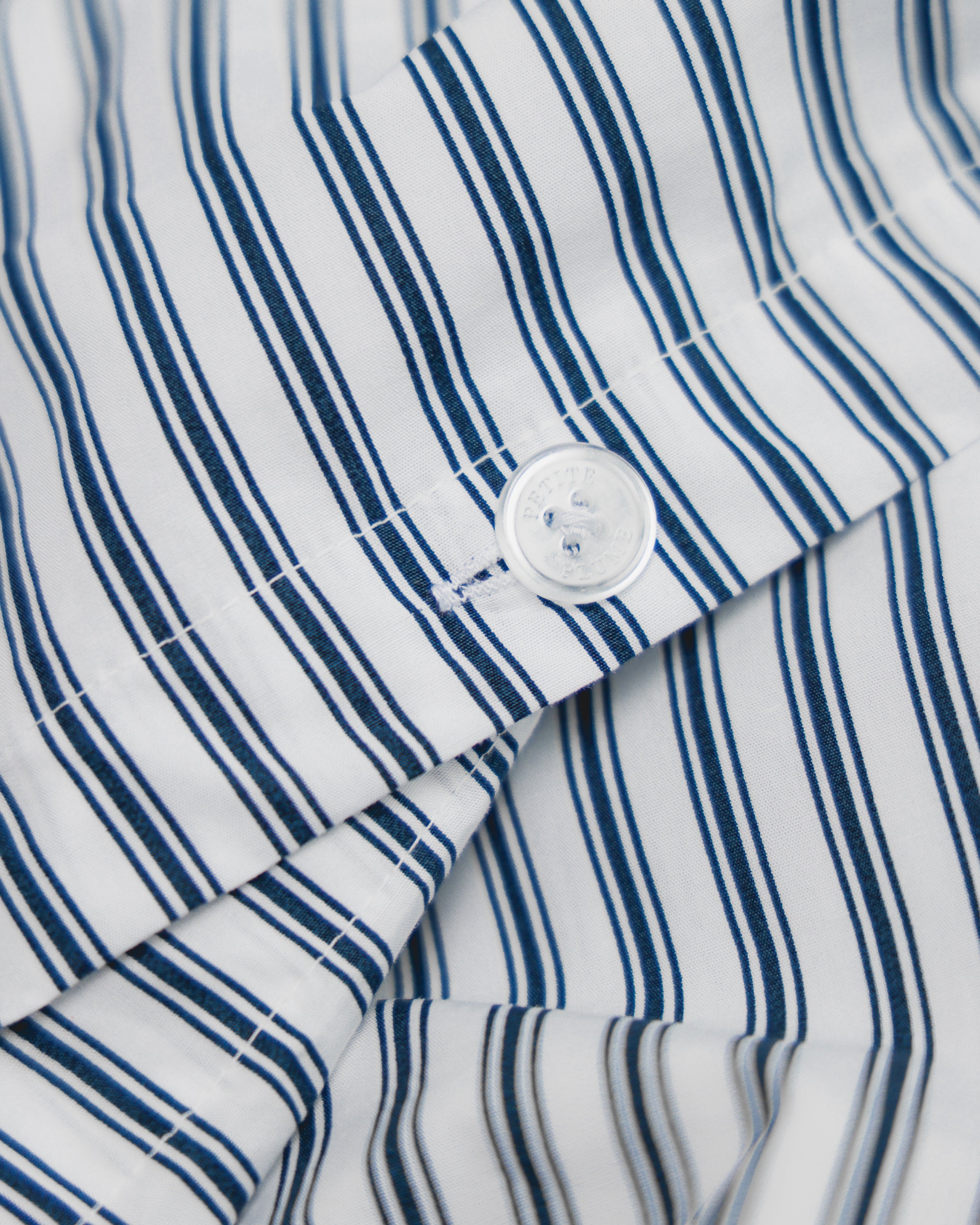 Close-up of Luxe Premium Percale Duvet Set in Navy French Ticking by Petite Plume, showcasing a cotton weave fabric with vertical navy and white stripes. A white button near intersecting stripes adds detail and texture, evoking the feel of luxury sheets.