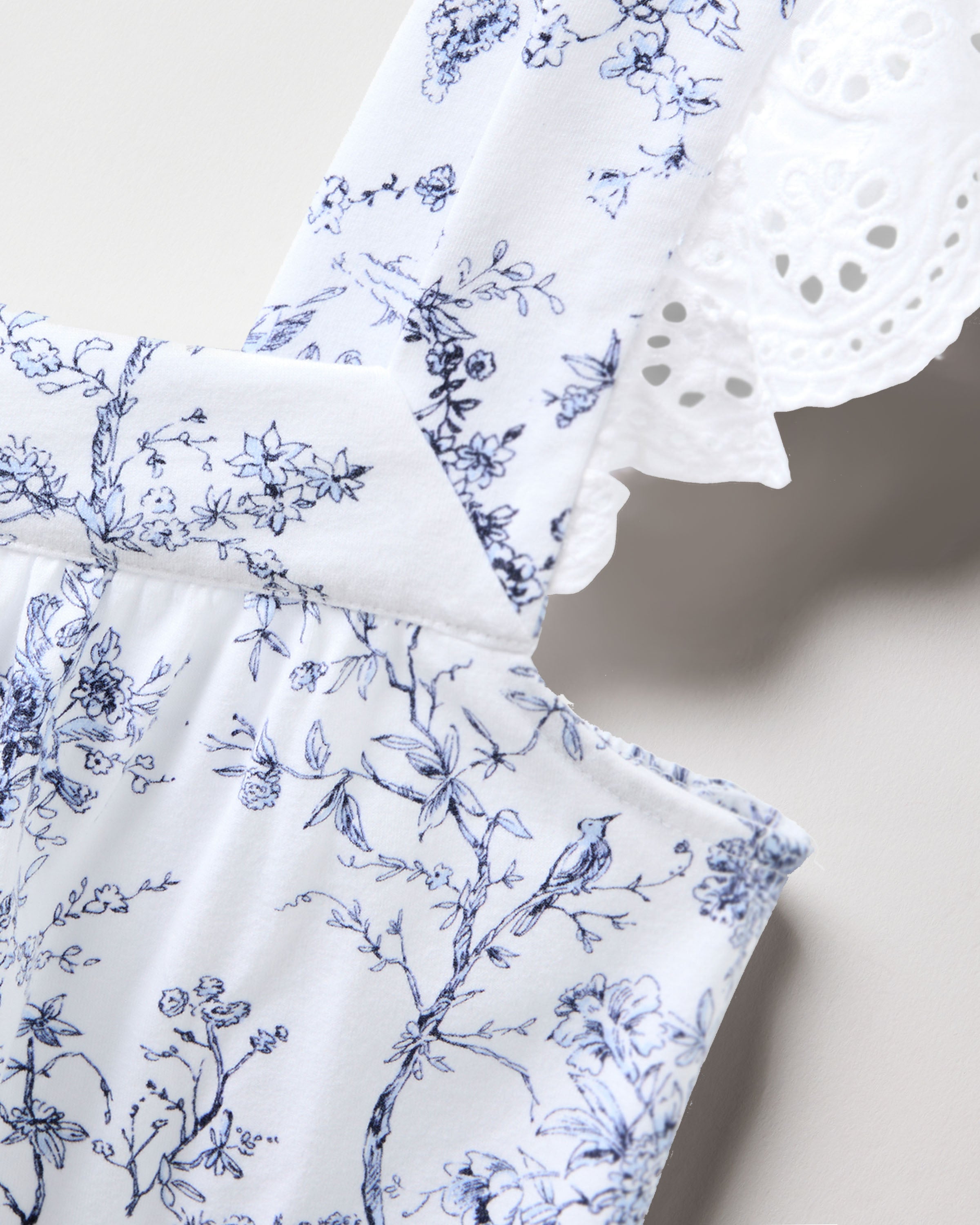 A close-up of the Womens Pima Clara Nightgown from Petite Plumes Timeless Toile collection reveals a delicate blue floral pattern with lace trim. The buttery smooth fabric, featuring birds and flowers on a light background, highlights elegance ideal for luxurious pajamas.