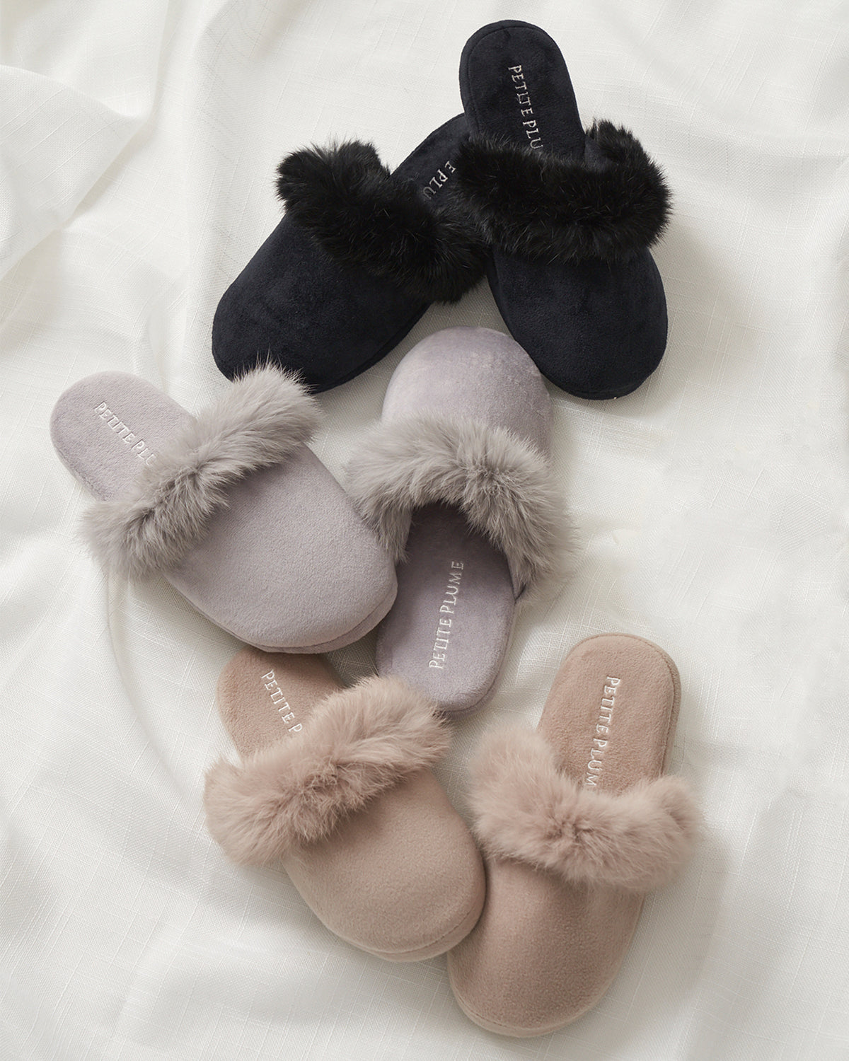 Three pairs of Petite Plumes Womens Faux Fur Trim Slippers sit on a white background, each a distinct color: black, gray, and beige. With their luxurious faux fur trim around the opening, these slippers perfectly complement any cozy sleepwear ensemble.