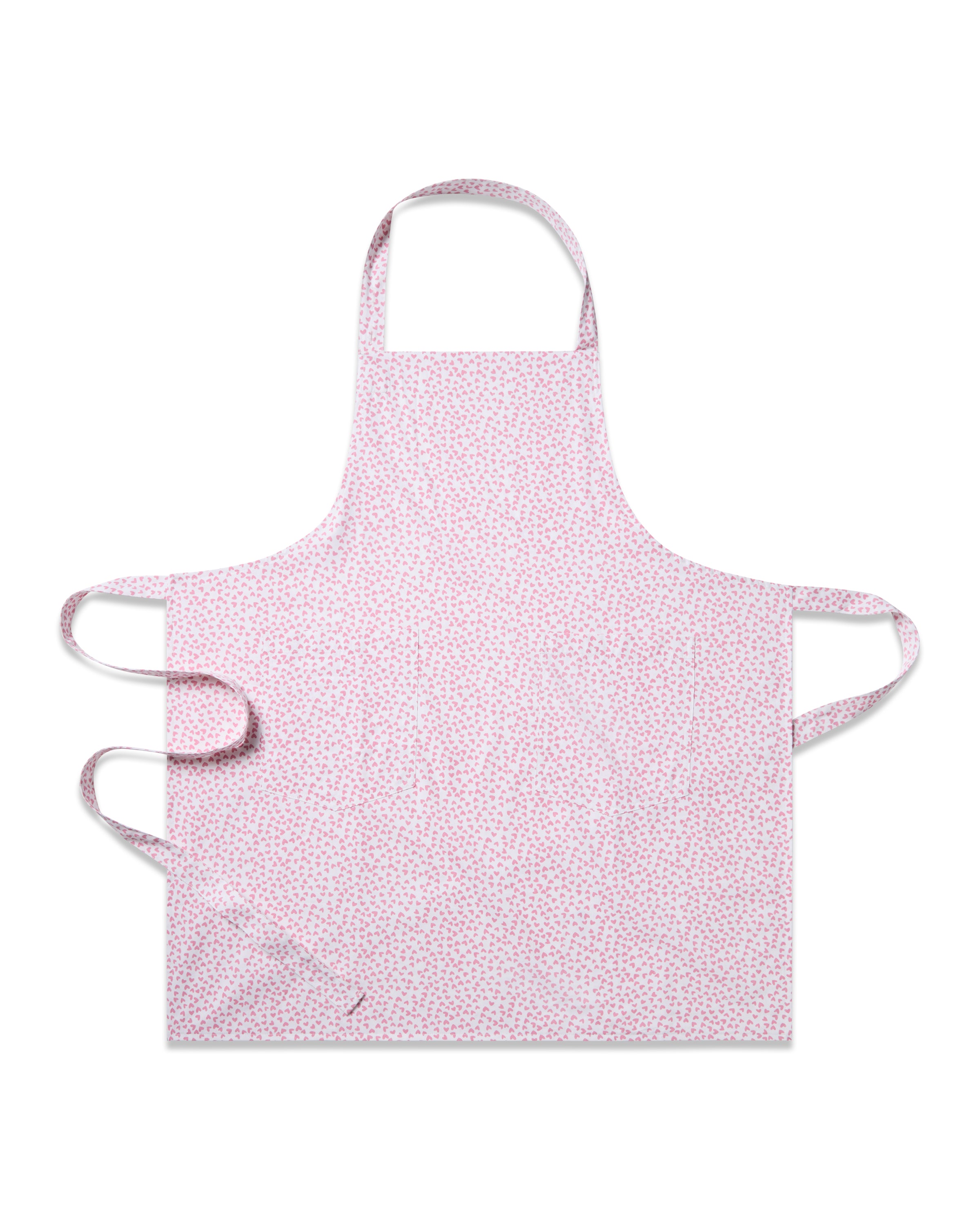 The Petite Plume Adult Apron in Sweethearts, featuring a subtle floral pattern and pink hearts, is displayed on a plain white background. This timeless piece has convenient neck and waist ties, combining style and functionality for any kitchen setting.