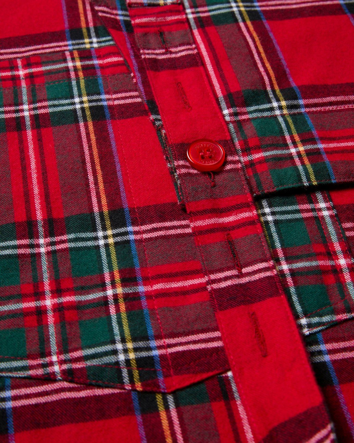 Close-up of Petite Plumes Kids Apron in Imperial Tartan, featuring a red plaid pattern with green, yellow, and white stripes and a charming red button, reminiscent of festive kitchen adventures.