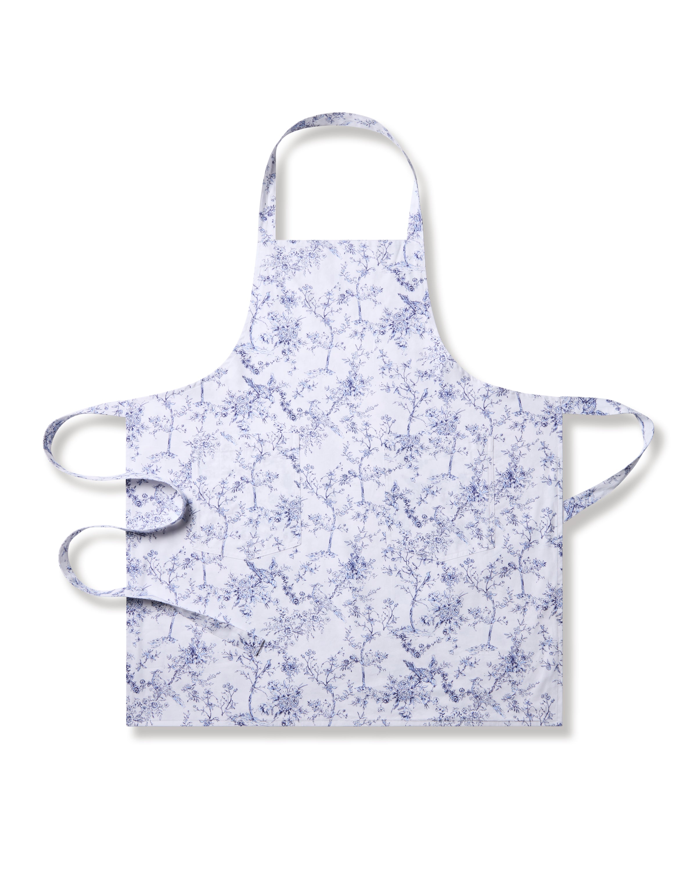 The Petite Plume Adult Apron in Timeless Toile showcases delicate blue floral patterns on white fabric, exuding botanical elegance. It features a neck loop and waist ties for a snug fit, making it perfect for holiday baking or any culinary activity with its simple yet elegant design.