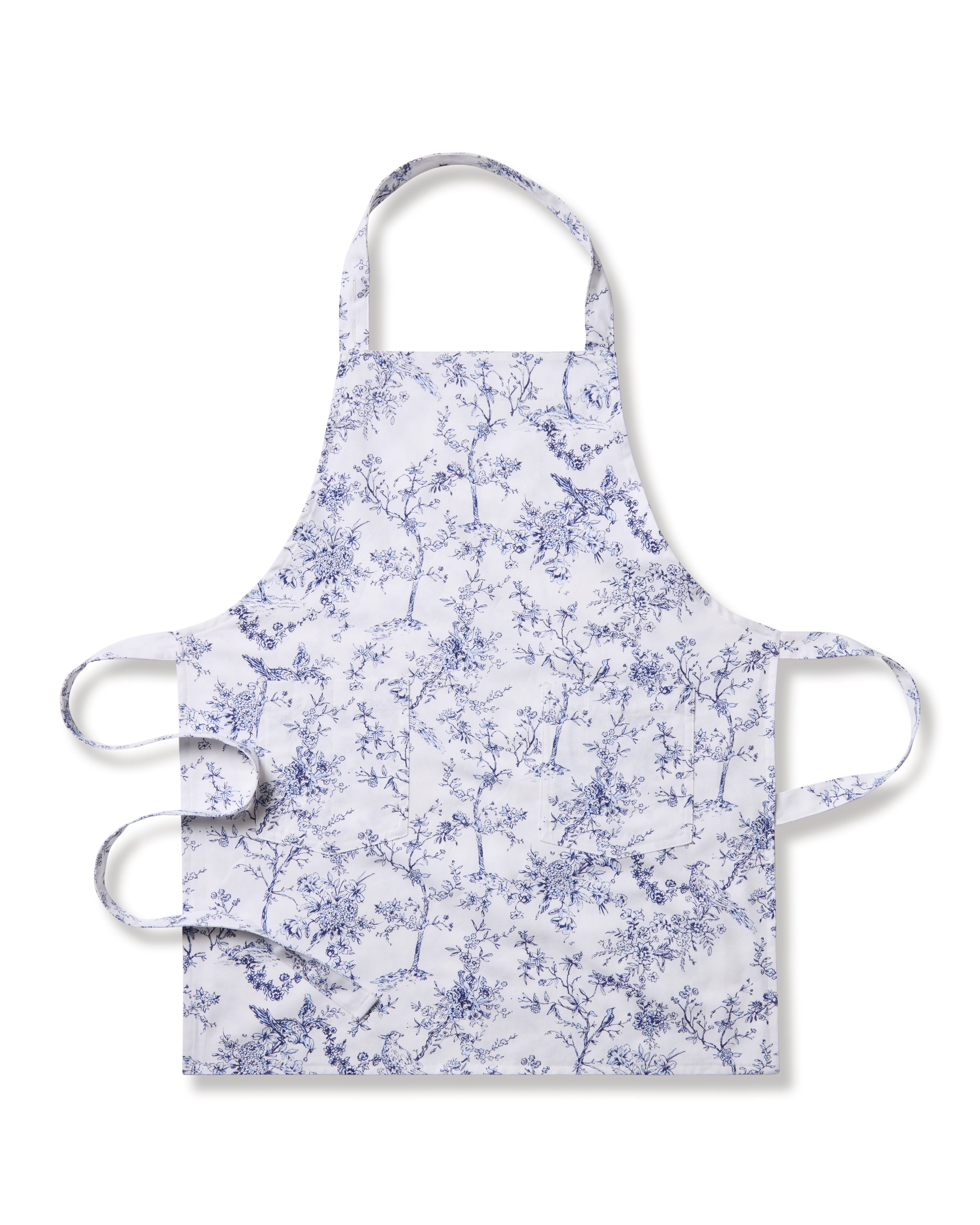 The Kids Apron in Timeless Toile by Petite Plume features a delicate blue floral pattern with branches and leaves. Ideal for holiday baking, it has an adjustable neck strap and waist ties, and the intricate design adds a touch of botanical elegance for a classic look.