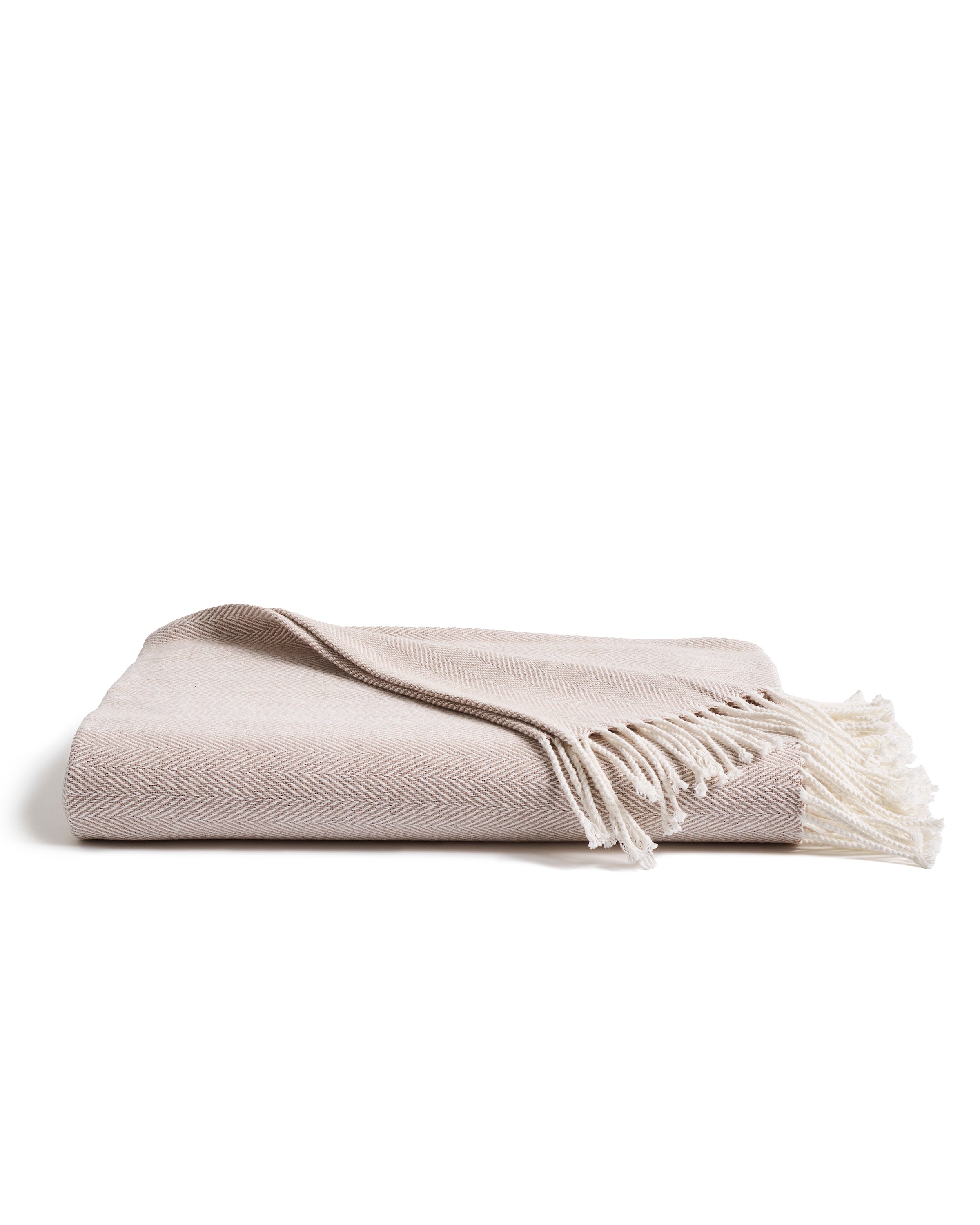 The Petite Plume Herringbone Throw in Beige, featuring fringed edges and a folded design on a white background, is perfect for elevating your home decor.