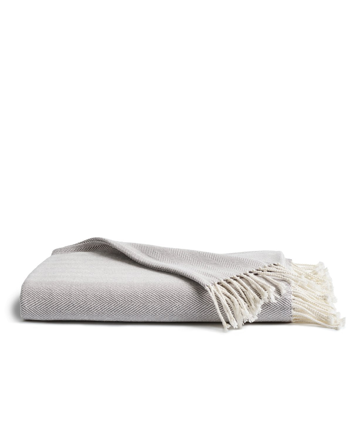 The Petite Plume Herringbone Throw in Light Grey is a folded cotton blanket with fringed edges, offering a soft and cozy texture. Its perfect for complementing various home decor styles and makes a thoughtful gift for any occasion.