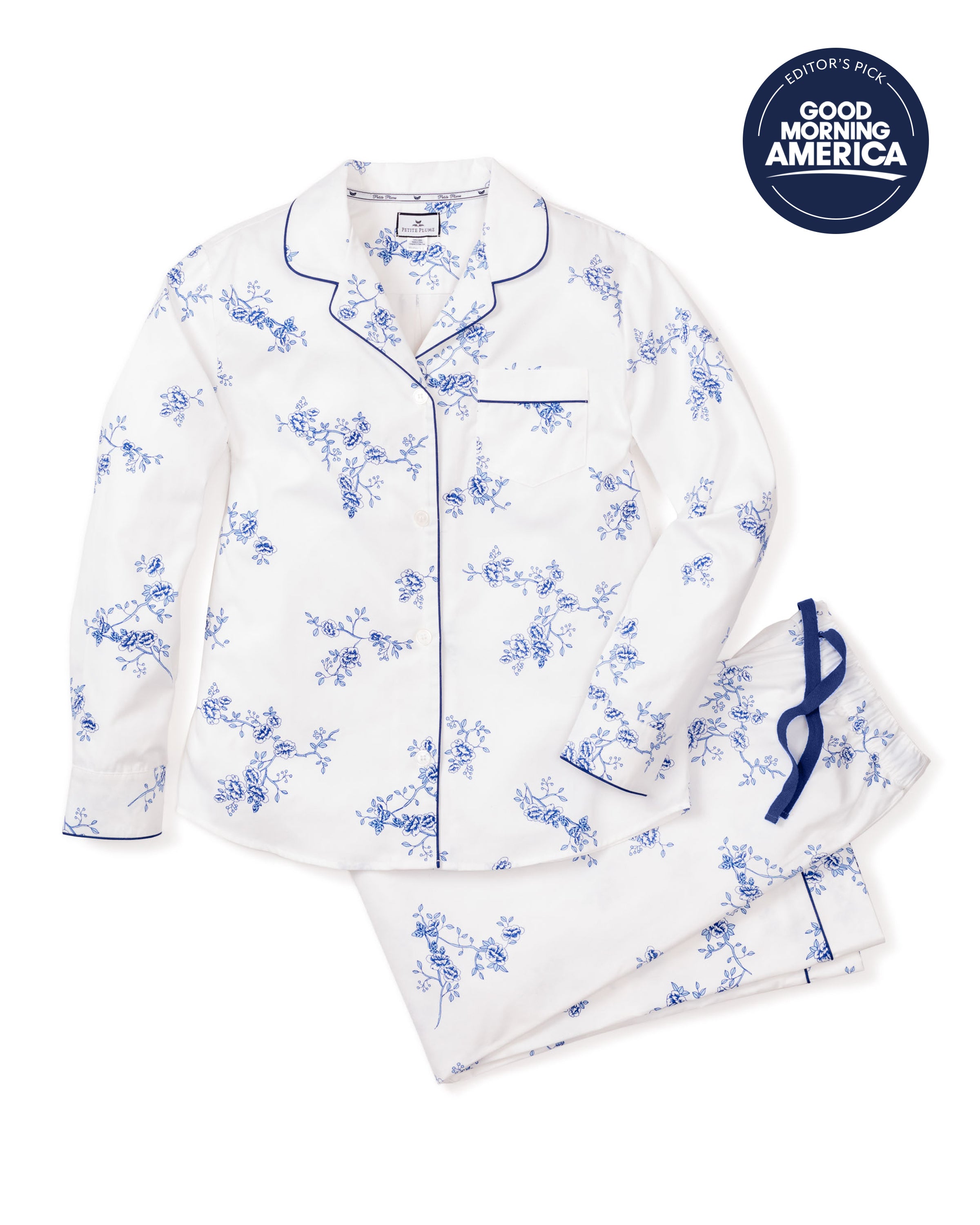 The Womens Twill Pajama Set in Indigo Floral by Petite Plume features a white pajama crafted from high-quality cotton with a blue floral pattern and elegant blue piping. It includes a long-sleeve top with buttons and chest pocket, drawstring pants, and carries a Good Morning America Editors Pick badge.