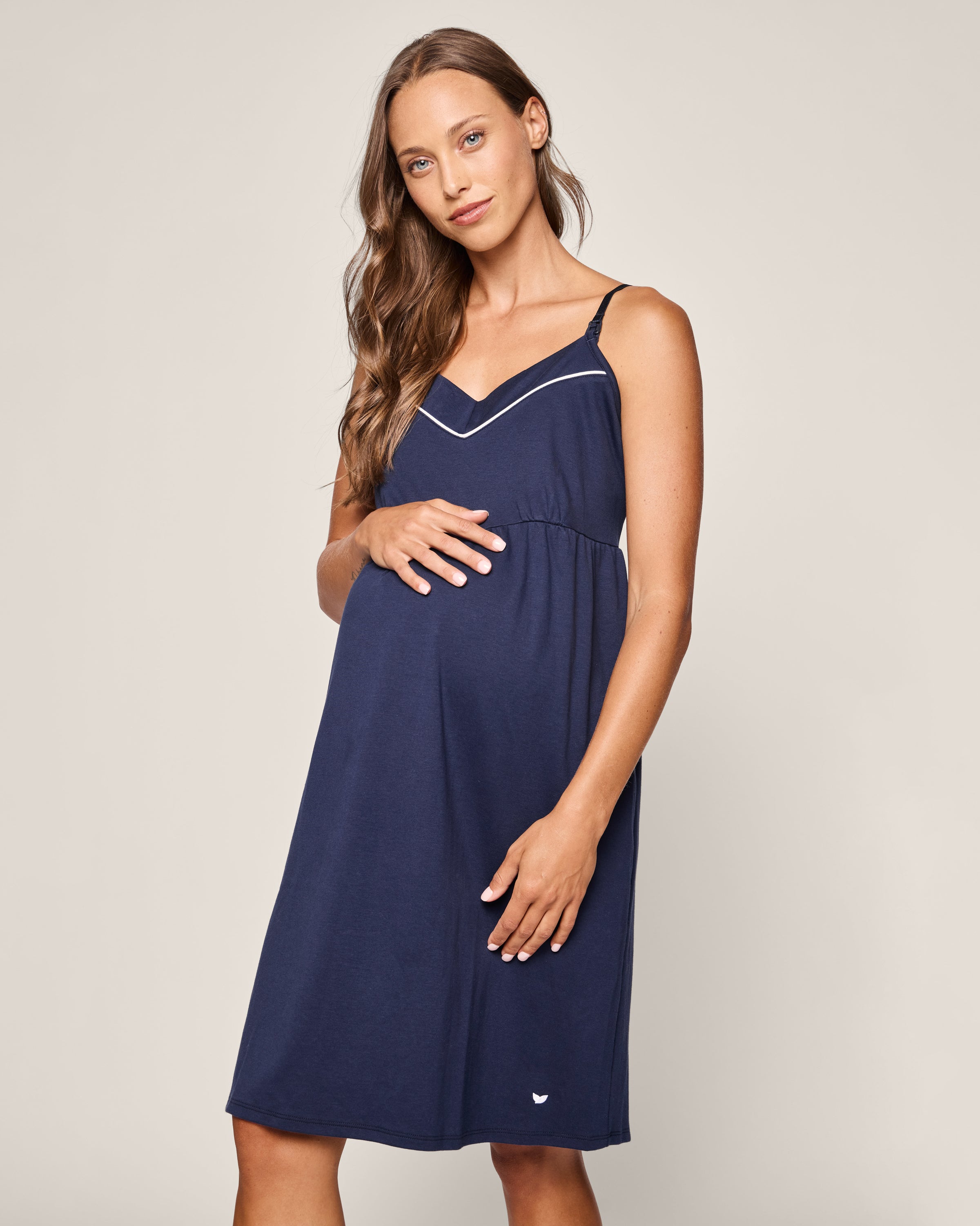 A pregnant woman, with long brown hair and a gentle smile, stands against a neutral background in Petite Plumes Womens Pima Maternity Nightgown in Navy, embodying the essence of pregnancy comfort.