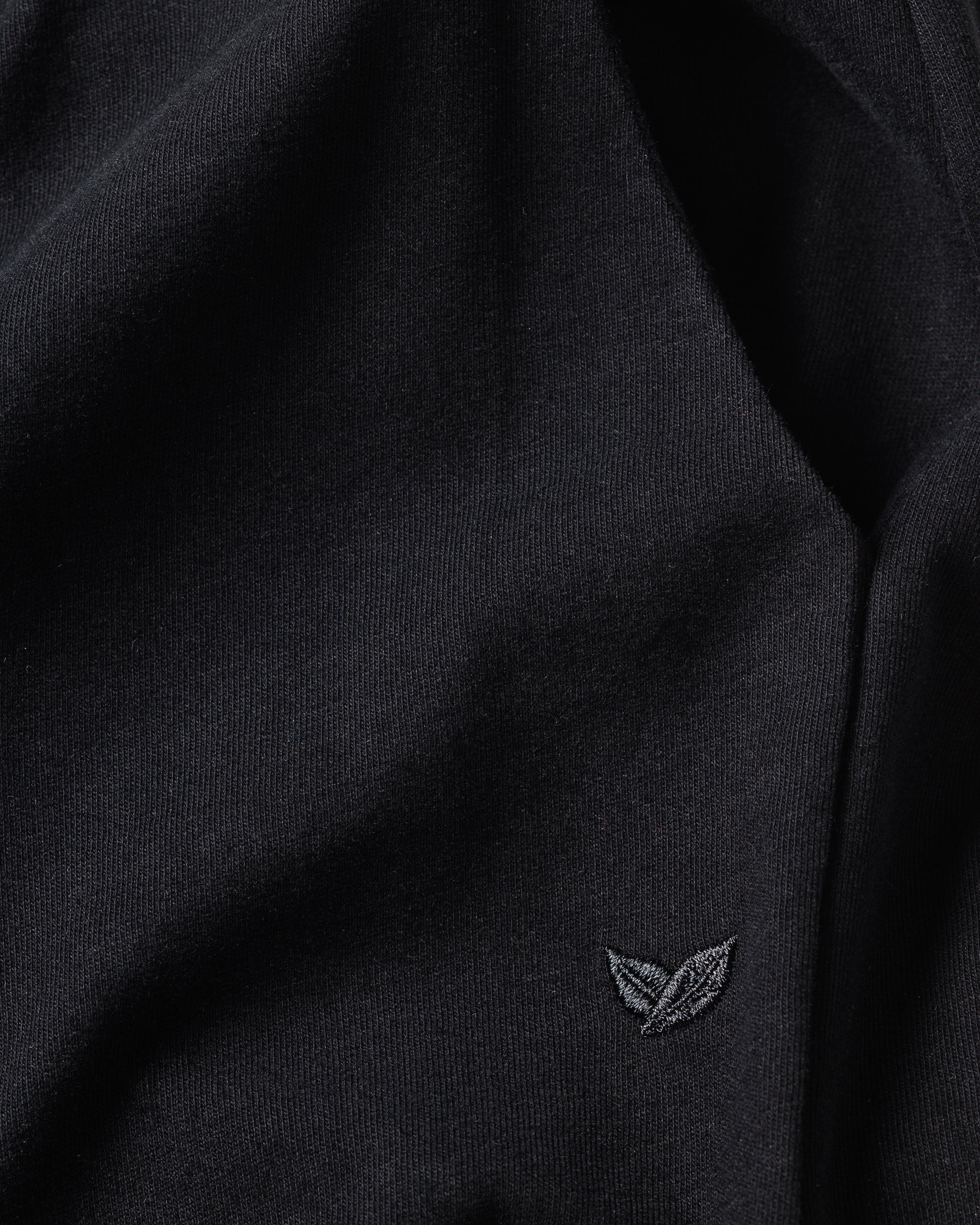 Close-up of the luxurious black Womens Pima Lounge Pants by Petite Plume, featuring a small embroidered leaf logo in the bottom right corner. The smooth texture suggests theyre crafted from Peruvian Pima cotton, hinting at their elegance.