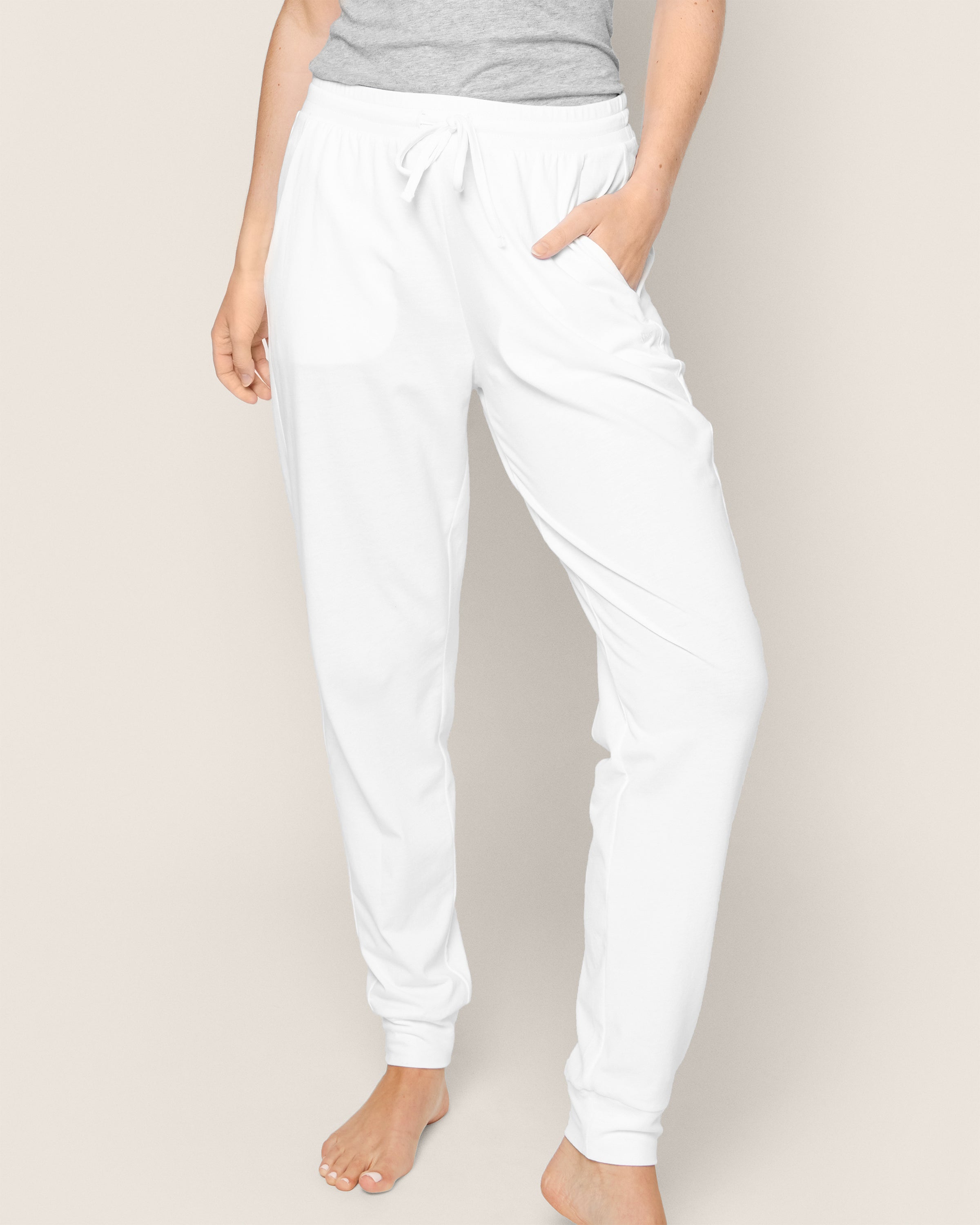 A barefoot individual models Petite Plumes luxurious Womens Pima Lounge Pants in White against a neutral backdrop, paired with a gray top. Made from Peruvian Pima cotton, this ensemble captures the essence of high-end sleepwear.