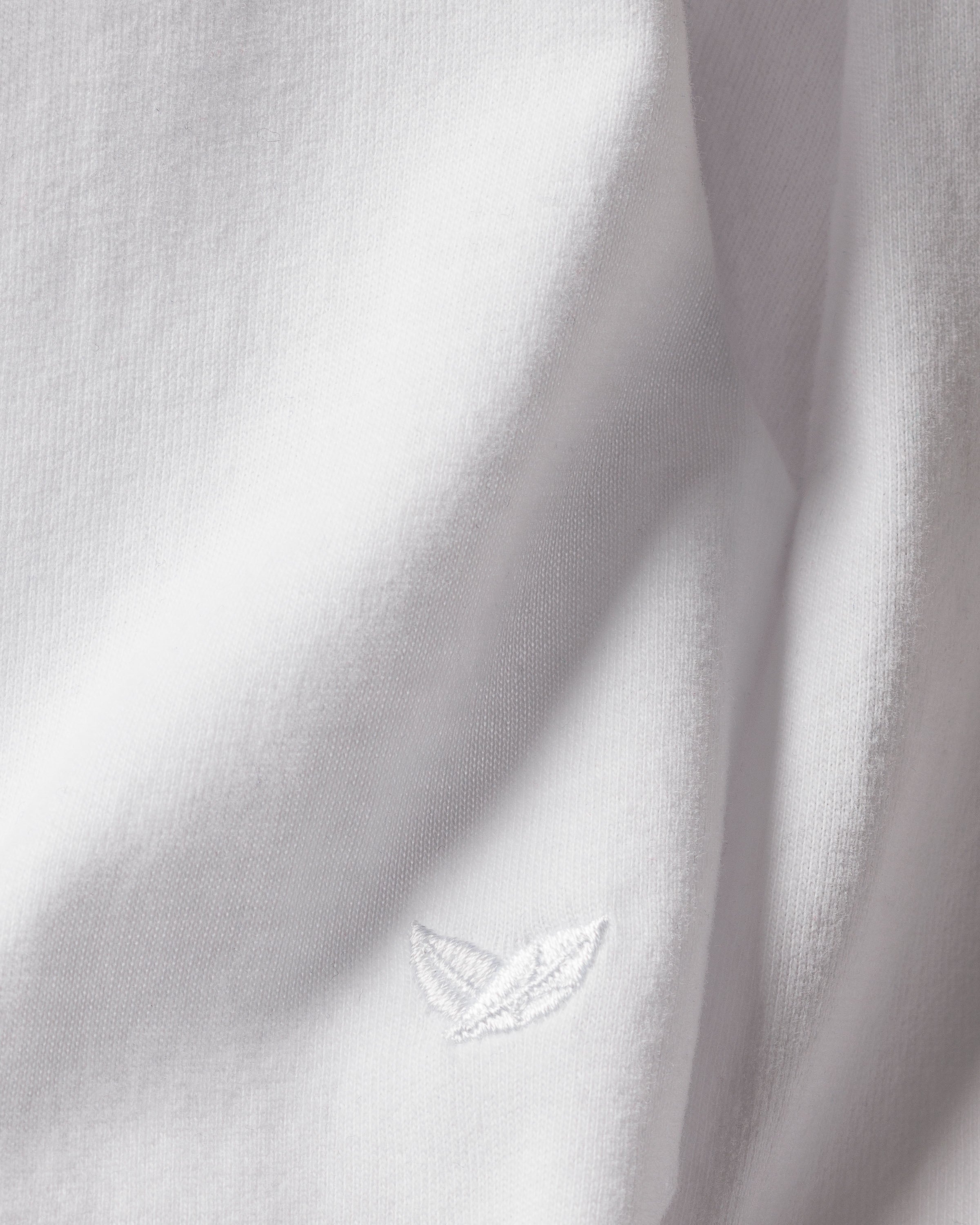 Close-up of Womens Pima Lounge Pants in White by Petite Plume, featuring a subtle embroidered logo with two overlapping leaves on exquisite Peruvian Pima cotton. The texture and stitching embody luxury pajamas, ideal for your bedtime ritual.