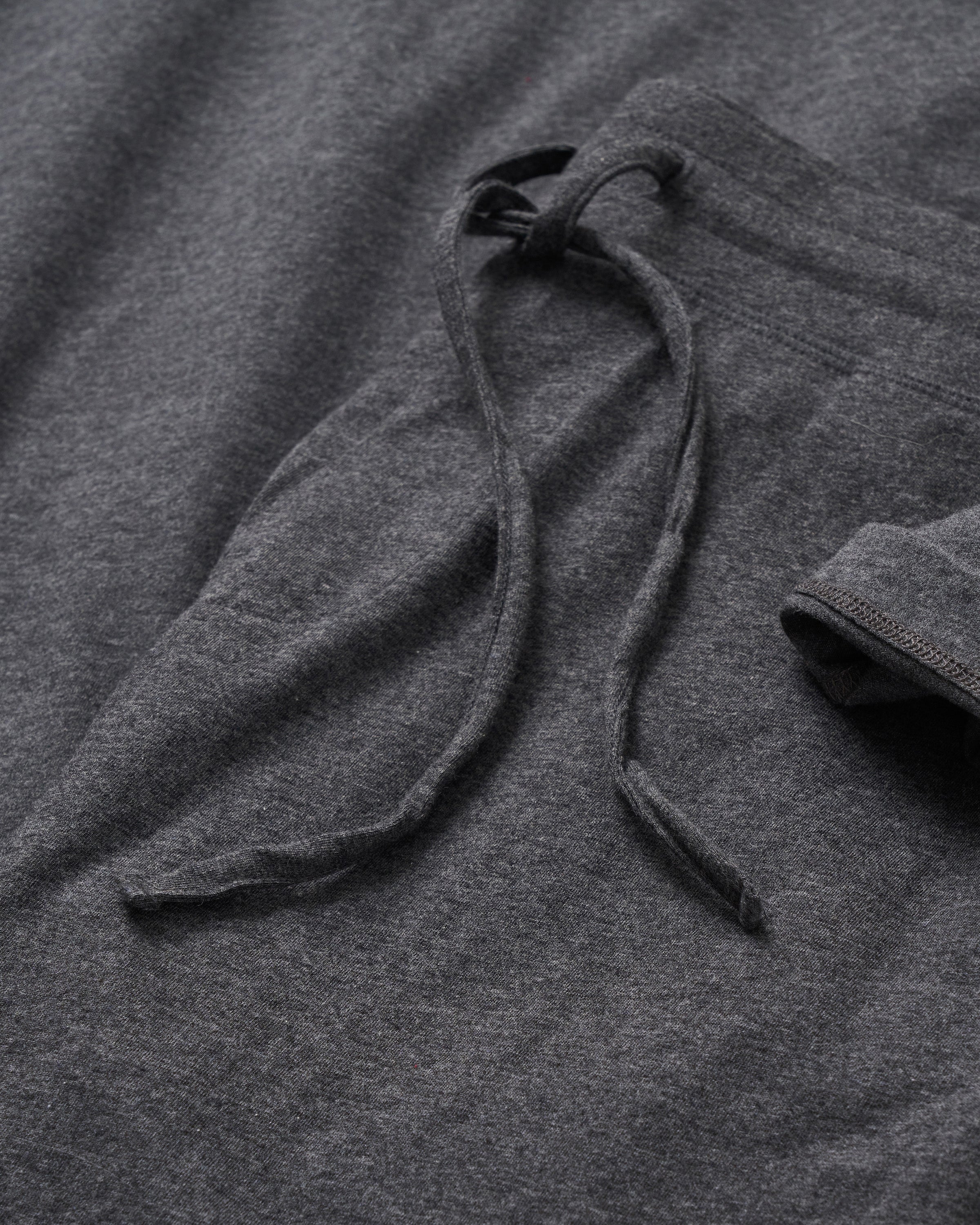 A close-up of the Mens Pima Pants in Dark Heather Grey by Petite Plume reveals a soft, slightly textured luxurious jersey knit, highlighted with a drawstring and partial sleeve design.