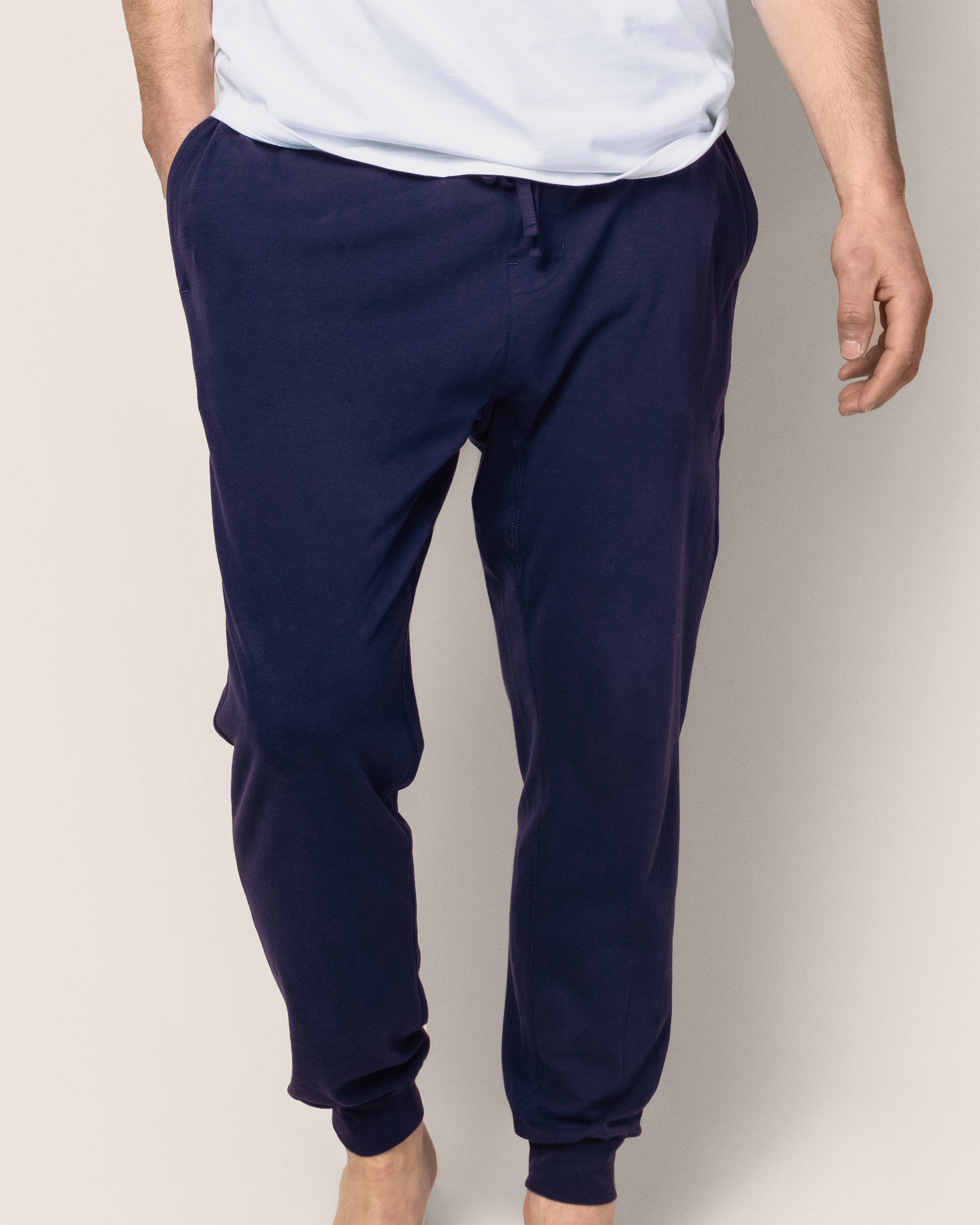 A person stands against a plain background in Petite Plumes Mens Pima Pants in Navy, crafted from jersey knit with a drawstring and visible pockets, paired with a soft white shirt. The luxurious pajamas-inspired look is complete without showing the persons face.