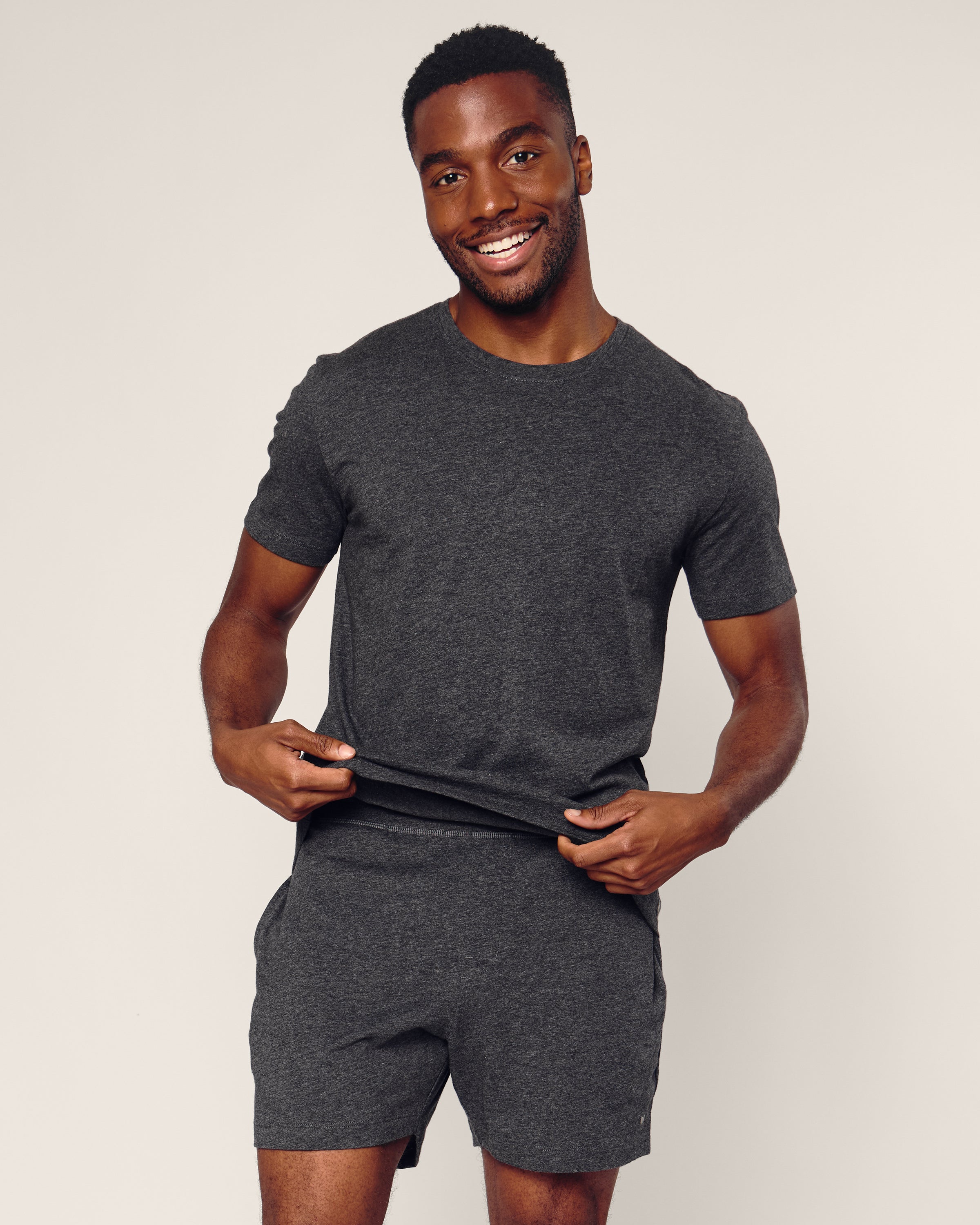 A man confidently poses against a light background wearing Petite Plumes Mens 5 Pima Shorts in Dark Grey, paired with a matching jersey knit t-shirt.