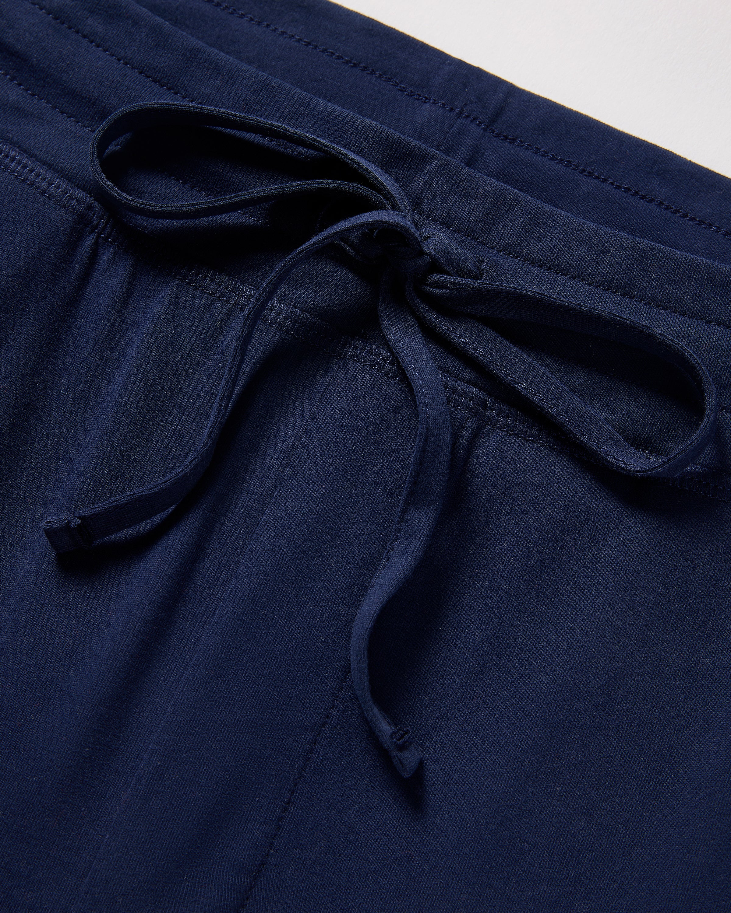 Close-up of Petite Plumes Mens 5 Pima Shorts in Navy, crafted from soft jersey knit. The shorts feature a drawstring waistband and lie on a light surface, exuding the comfort and luxury of pajamas.