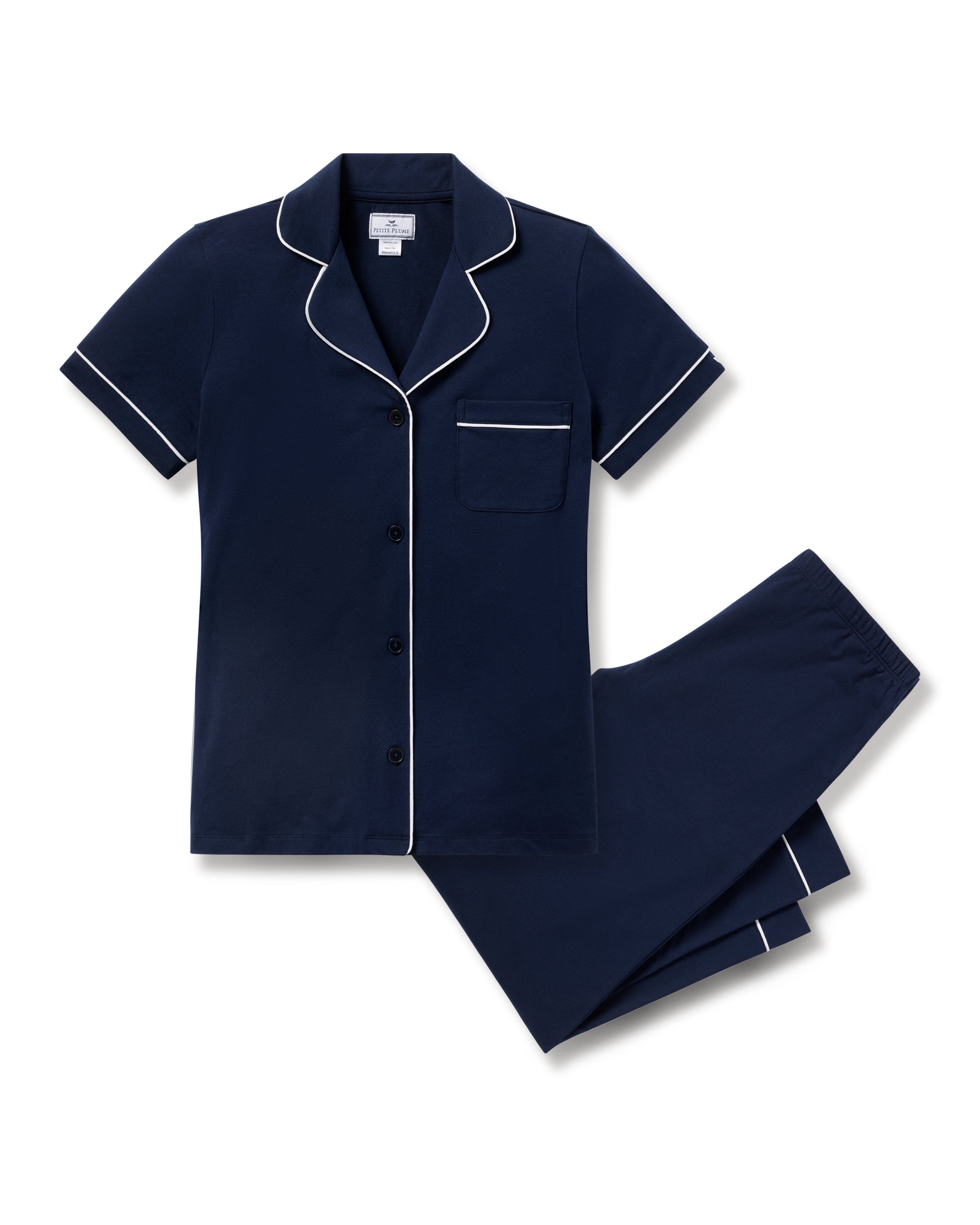 The Womens Pima Crop Set by Petite Plume is a luxury sleepwear ensemble crafted from Peruvian Pima cotton. It features a navy blue short-sleeve collared button-up top with white piping and matching pants with an elastic waistband, presented on a plain white background.