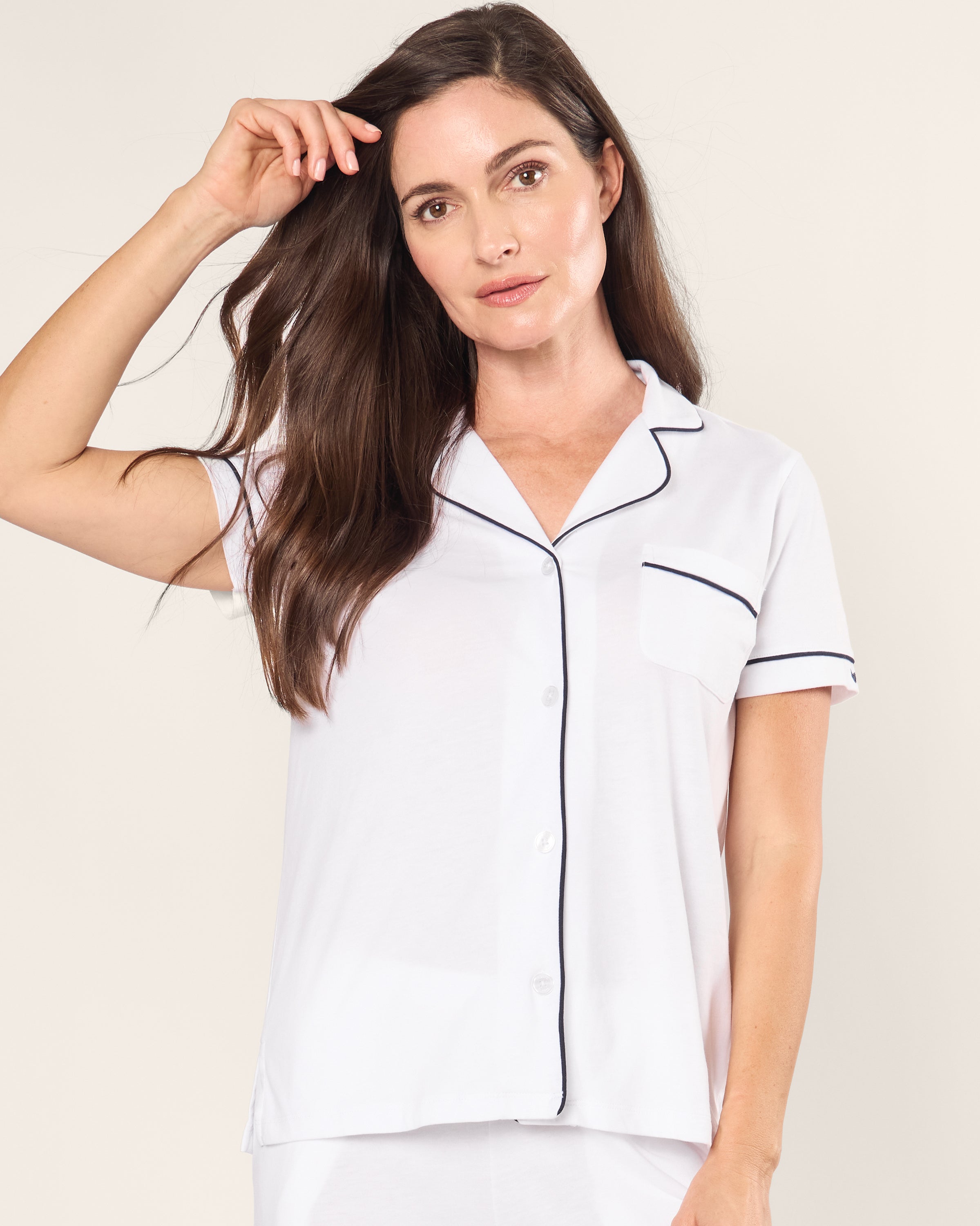 A person with long brown hair wearing a Petite Plume Womens Pima Crop Set in white with navy piping holds their hair, exuding a breathable feel against the plain, light background.