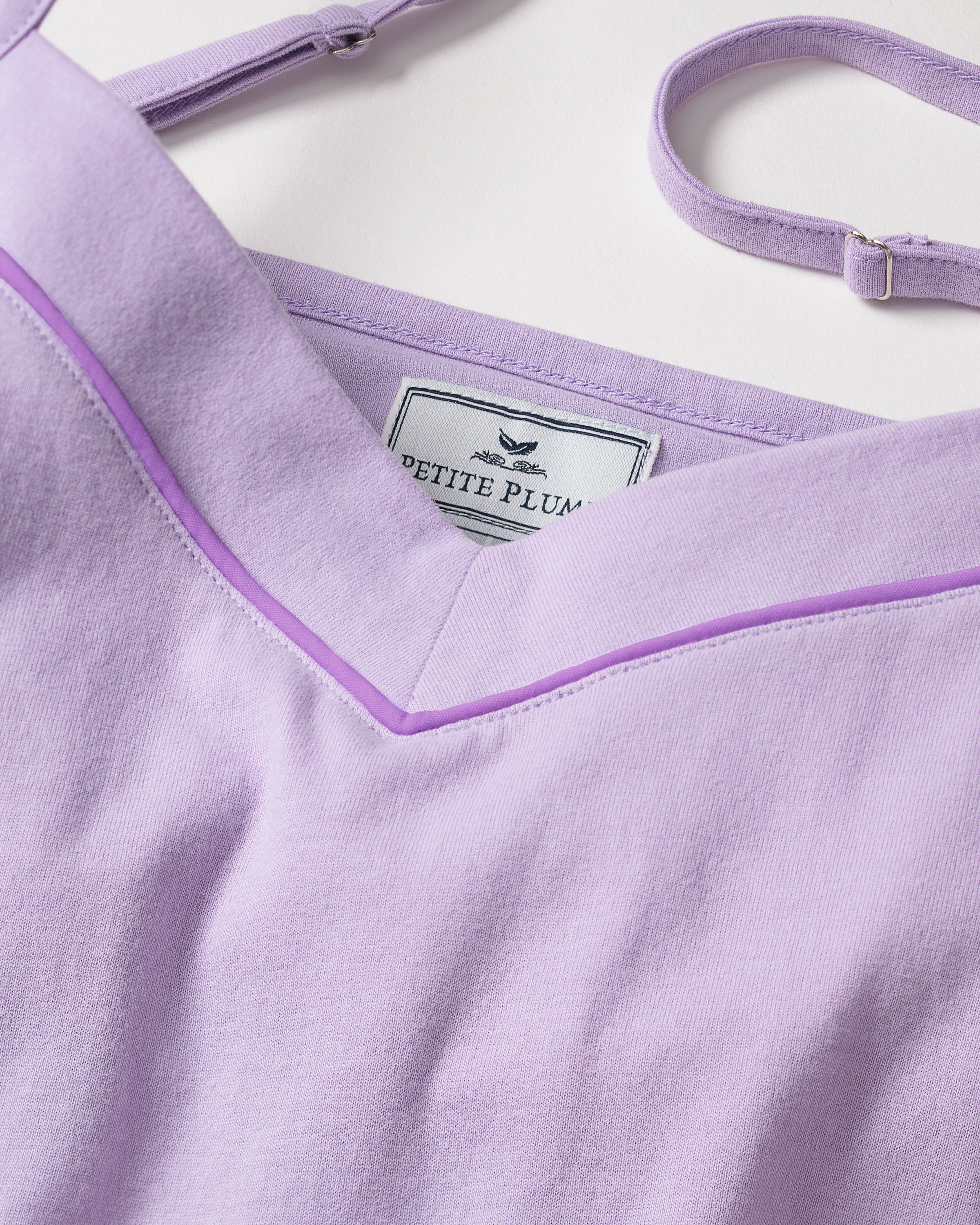 Close-up of the Womens Pima Sylvie Cami Short Set in Lavender by Petite Plume, showcasing a v-shaped neckline with light purple trim. The luxurious Pima cotton fabric offers a smooth, soft texture. An adjustable strap and the brand label are also shown.