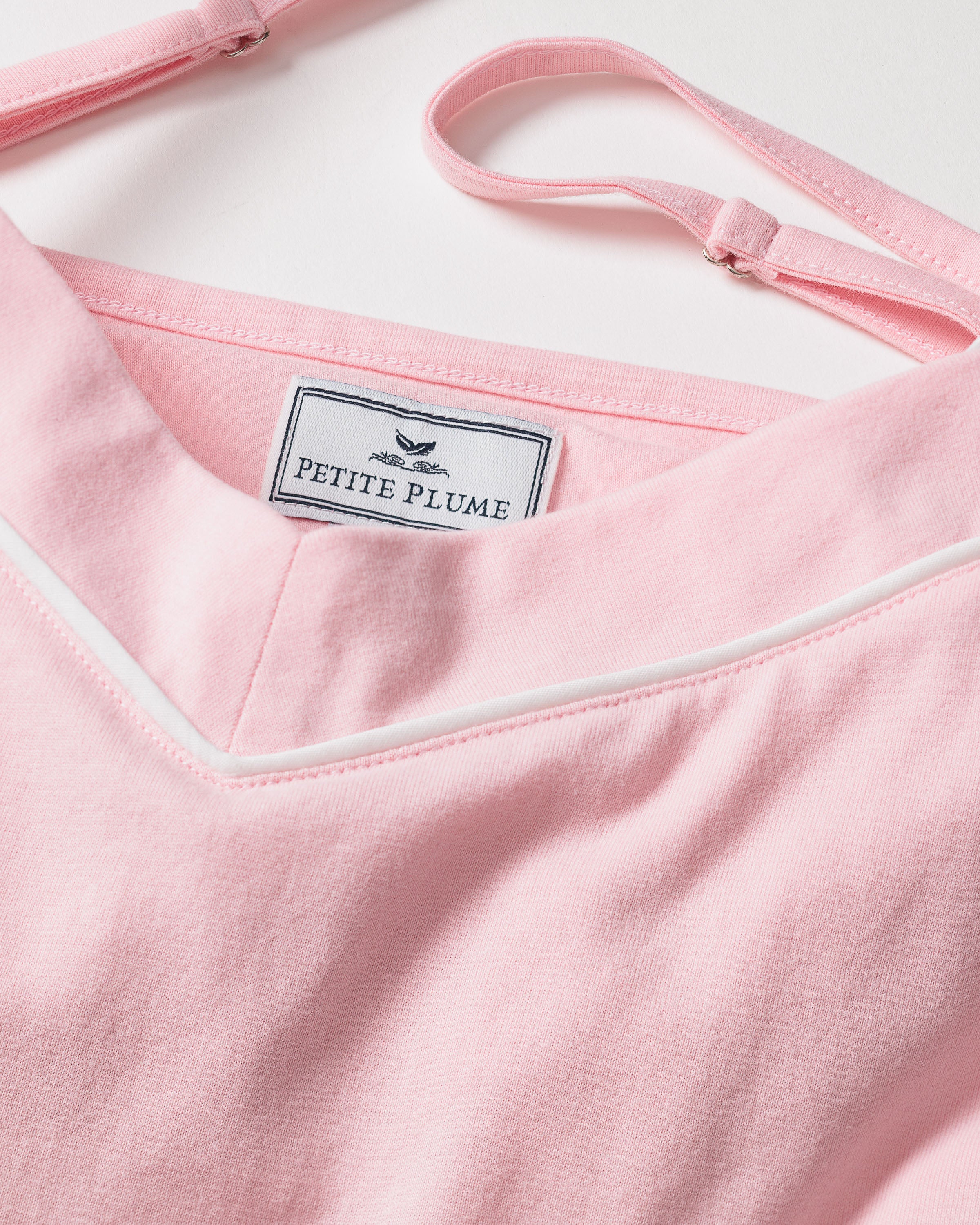 A close-up of the Womens Pima Sylvie Cami Short Set in Pink by Petite Plume reveals its luxurious soft Pima cotton, V-shaped neckline with white trim, and adjustable straps, suggesting its comfortable yet elegant sleepwear.