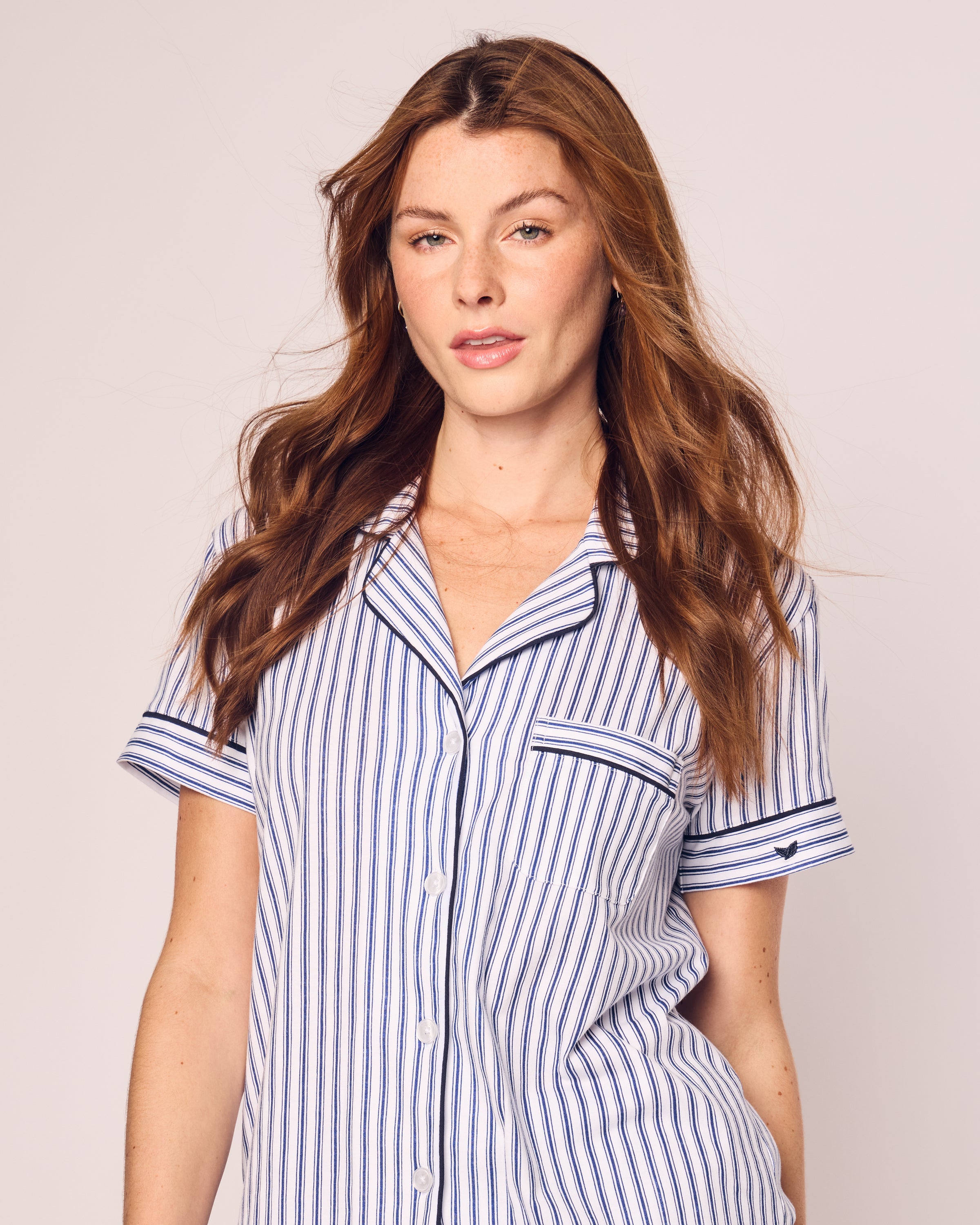 A person with long, wavy brown hair is wearing Petite Plumes Womens Pima Pajama Short Set in Navy French Ticking. They stand against a plain background.