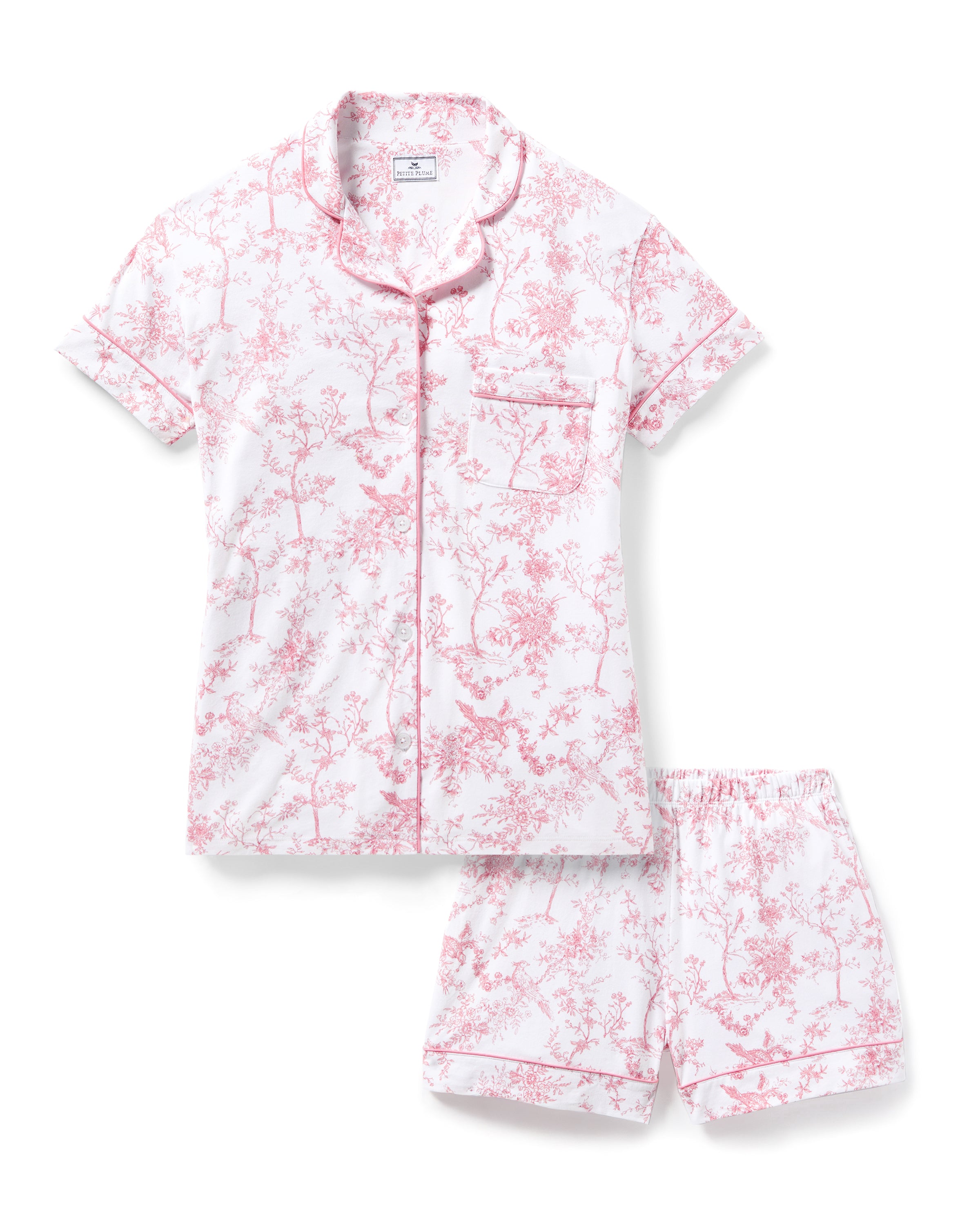 The Womens Pima Short Sleeve Short Set in Pink Timeless Toile by Petite Plume features a white background with pink floral designs, a top with a chest pocket and pink piping, and shorts with an elastic waistband. This delicate, feminine set offers botanical elegance for luxurious relaxation.