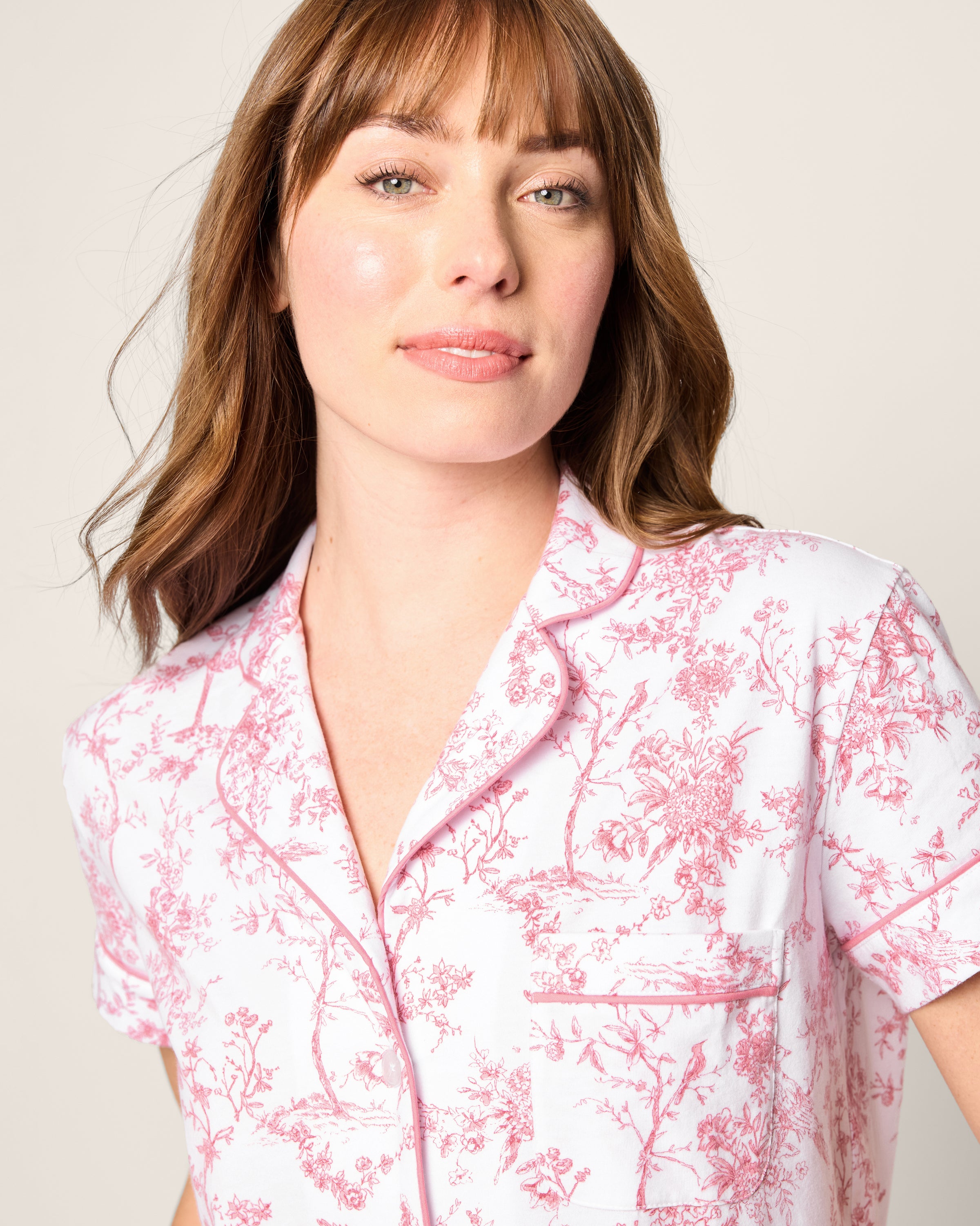 A person with shoulder-length brown hair is wearing Petite Plumes Womens Pima Short Sleeve Short Set in Pink Timeless Toile, exuding botanical elegance against a plain background.