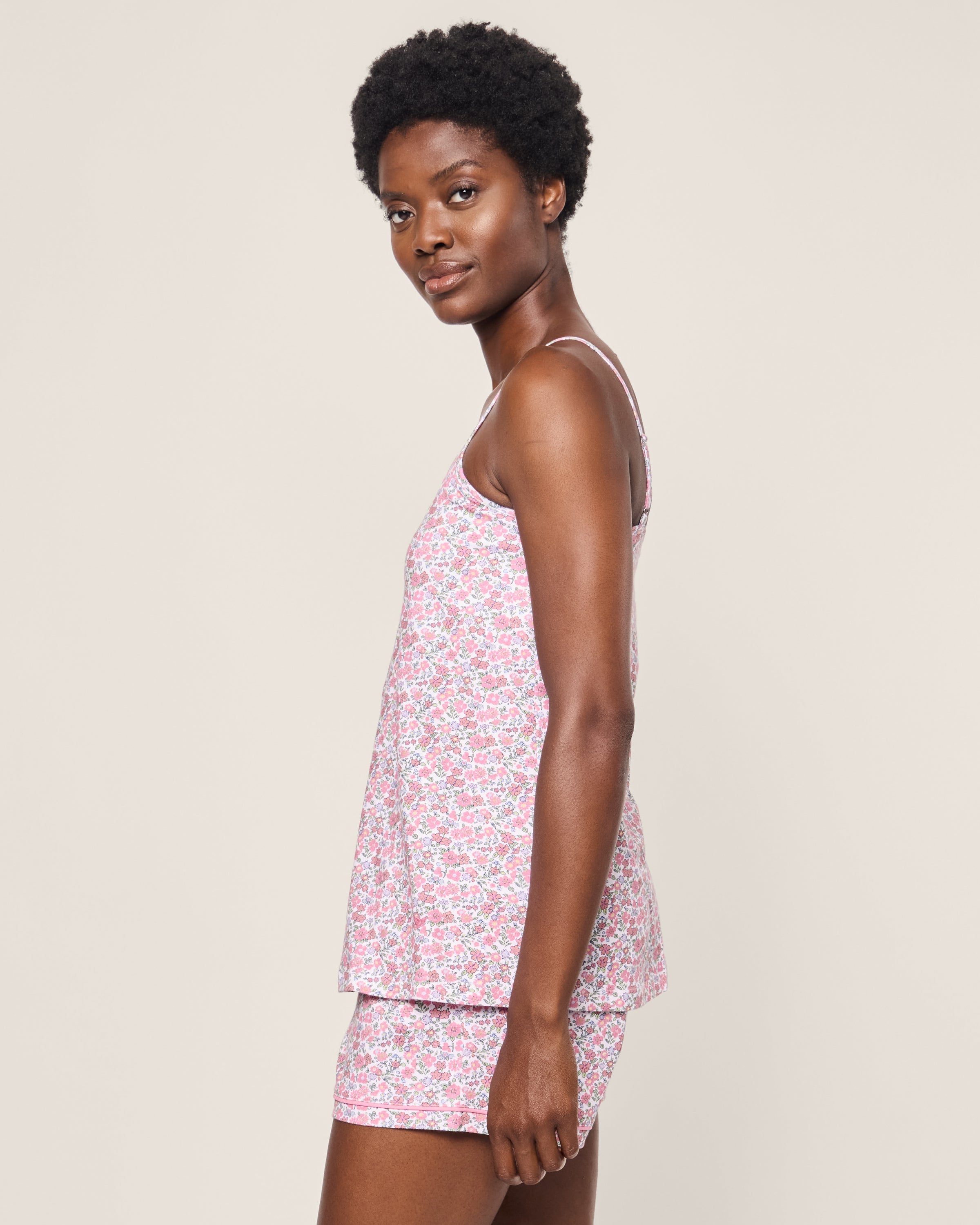 A person with short curly hair models Petite Plumes Womens Pima Sylvie Short Set in Fleurs de Rose, including a tank top and shorts. They stand sideways against a plain background, gazing at the camera.