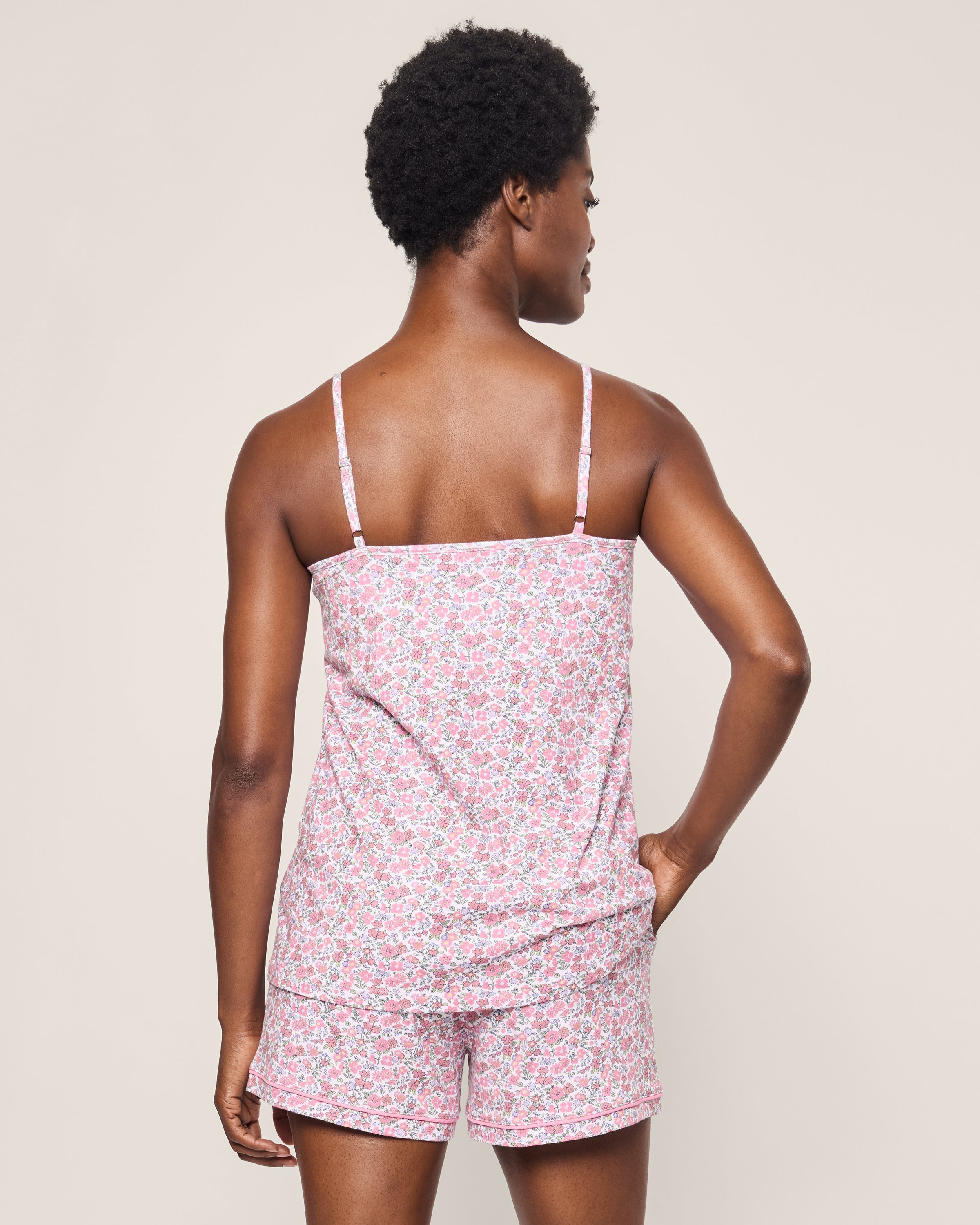 A person stands with their back to the camera, wearing the Womens Pima Sylvie Short Set in Fleurs de Rose by Petite Plume. The background is a plain light color.