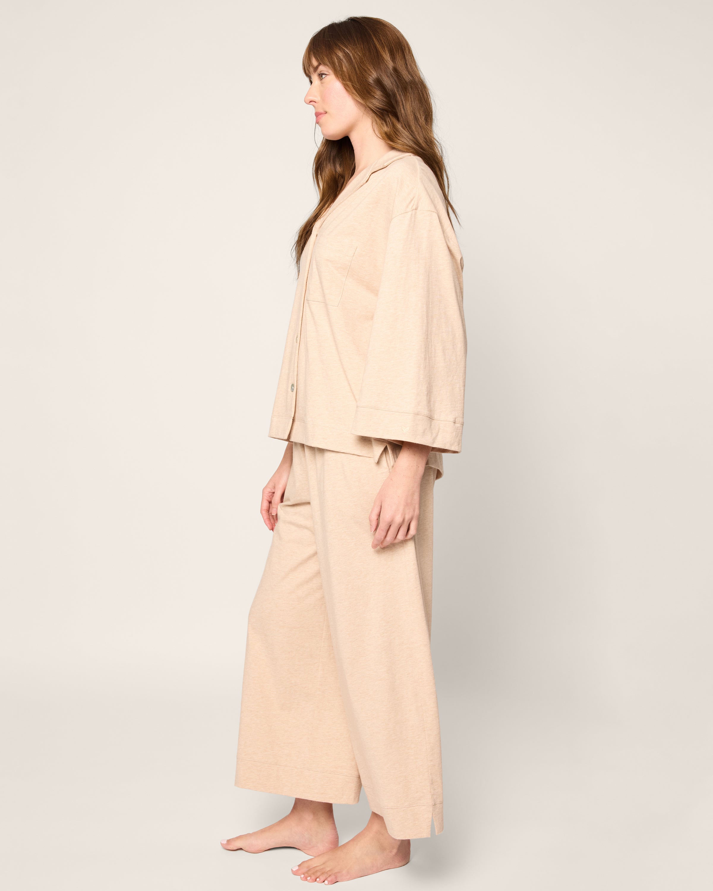 A person with long brown hair, in profile against a light background, is barefoot and wearing the loose-fitting Petite Plume Olivia Wide Leg Pima Pajama Set in Camel.