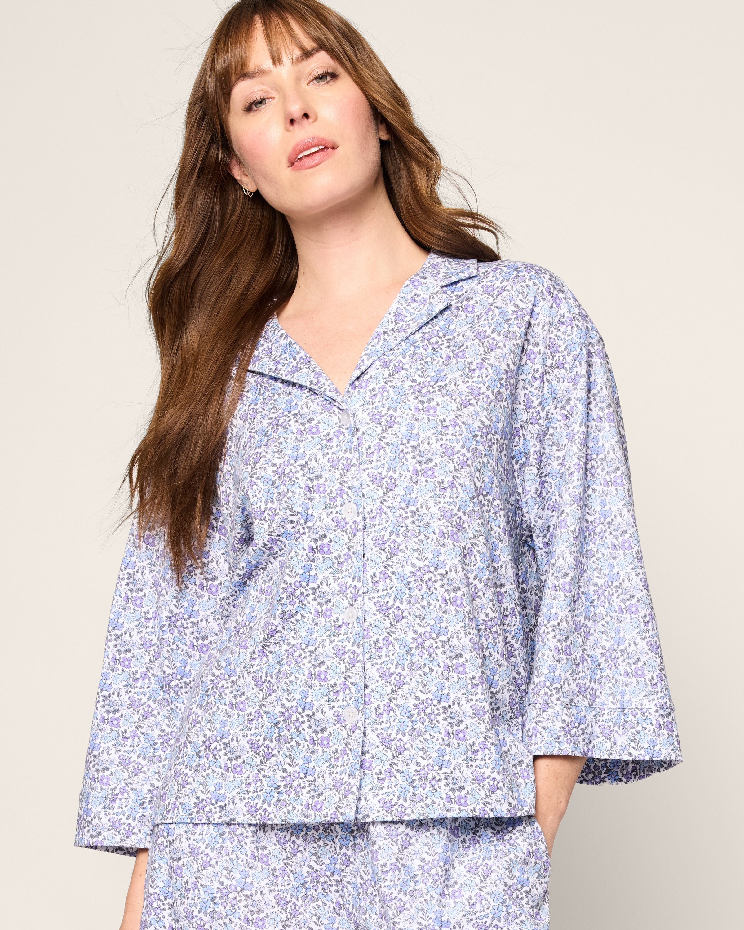 A person with long brown hair wears The Olivia Wide Leg Pima Pajama Set in Fleur dAzur by Petite Plume, known for its luxurious Peruvian Pima cotton. The wide sleeves beautifully complement the style against a plain, neutral background.