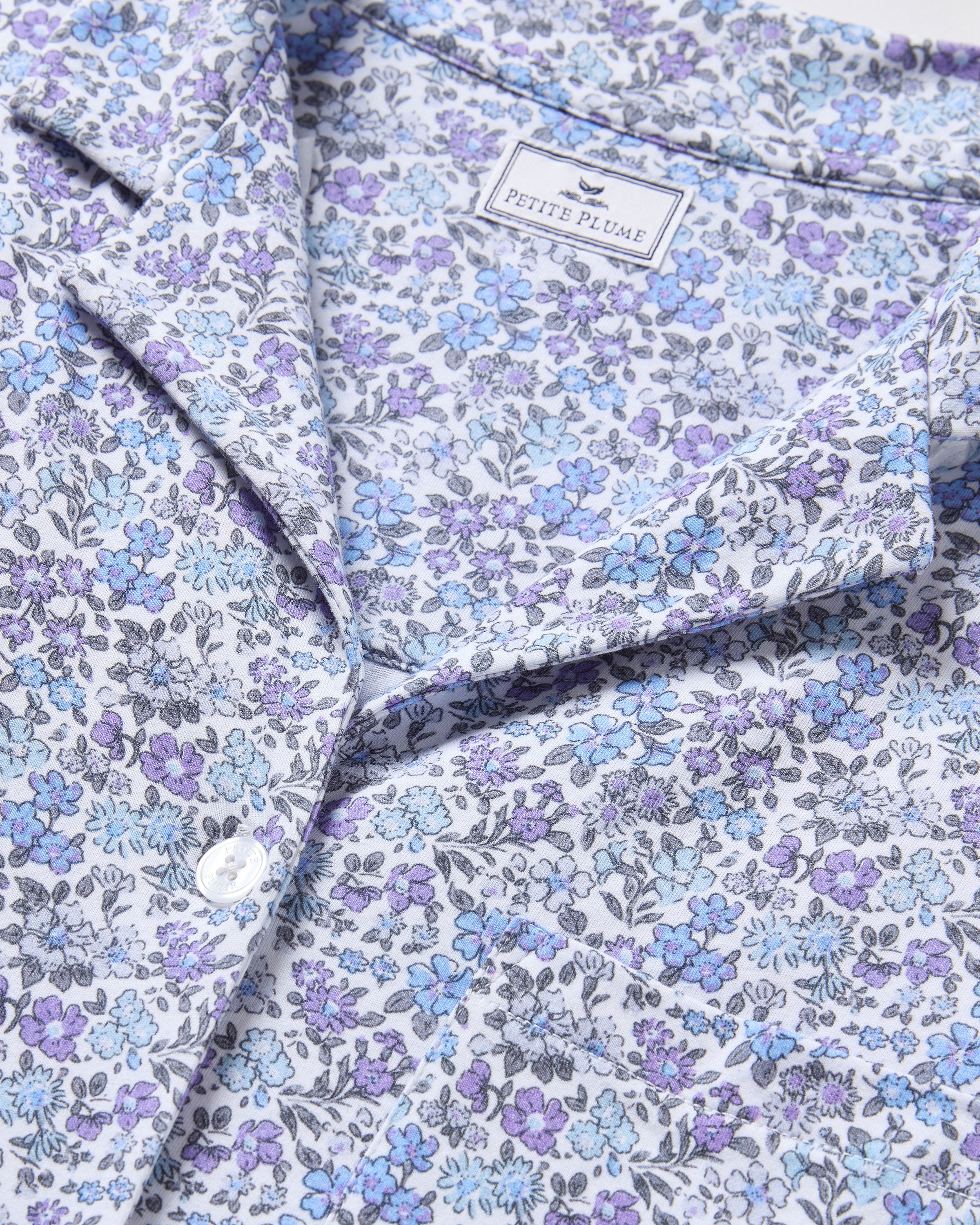 Close-up of The Olivia Wide Leg Pima Pajama Set in Fleur dAzur, crafted from luxurious white Peruvian Pima cotton with a floral pattern in blue and purple, featuring button closure and a Petite Plume tag.