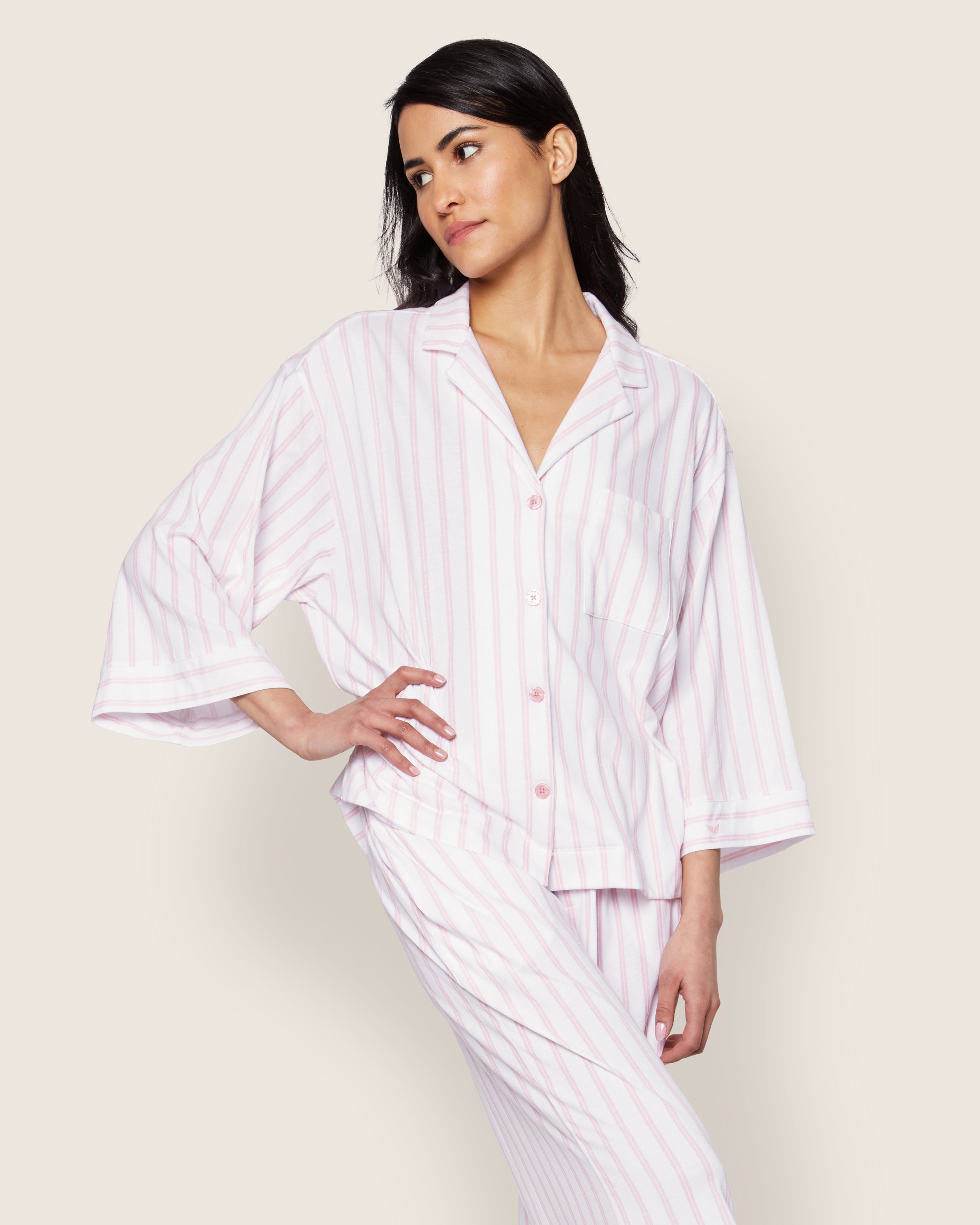 A person in a Petite Plumes Olivia Wide Leg Pima Pajama Set in Pink Stripe poses against a plain background. The luxurious set features a light pink, white-striped top with collar and buttons, while the pants offer a relaxed fit for ultimate comfort.