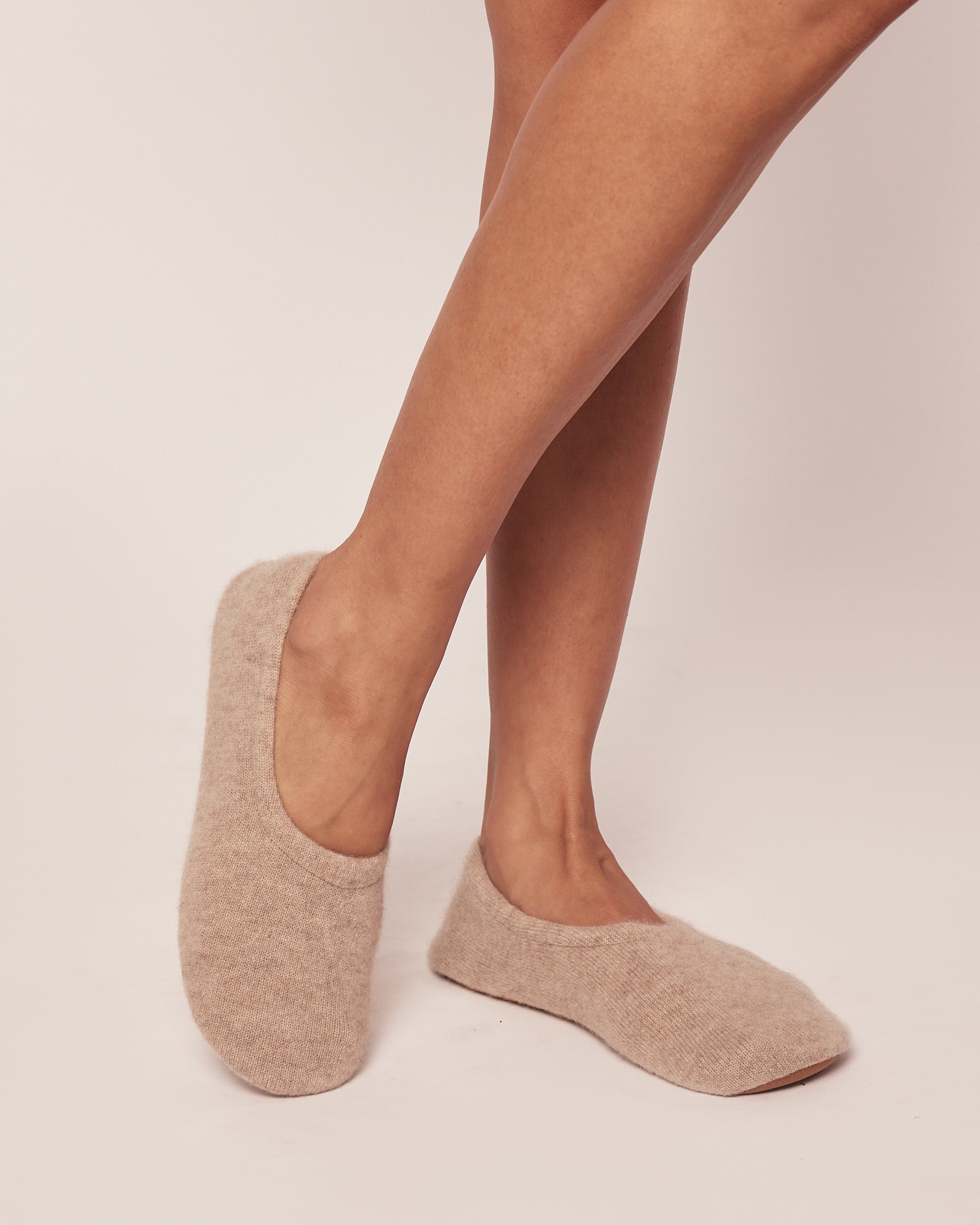 Close-up of legs in Petite Plume Womens Cashmere Slippers in Beige, showcasing their cozy, open-top design and soft cashmere against a neutral background.