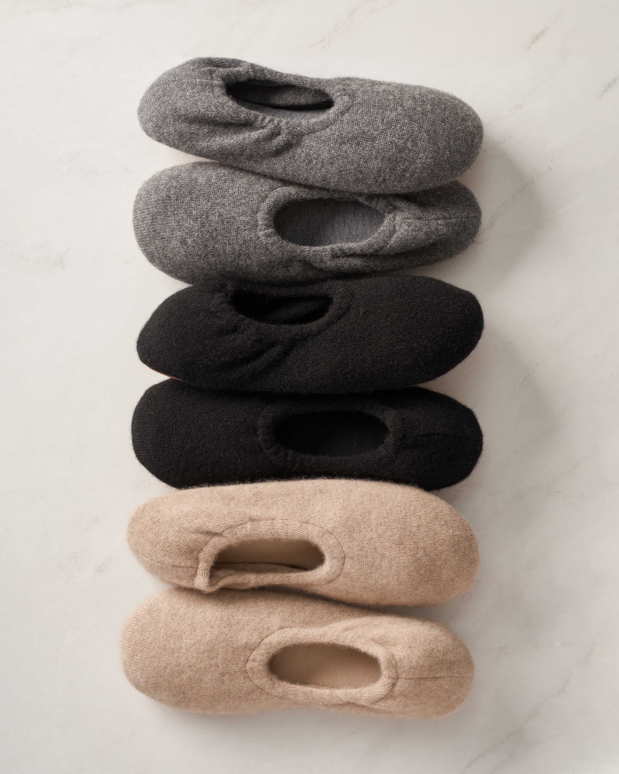 Five pairs of Petite Plume slippers are arranged vertically: dark gray, light gray, black, solid black, and beige. The Womens Cashmere Slippers in Beige add a touch of luxury with their irresistibly soft texture.