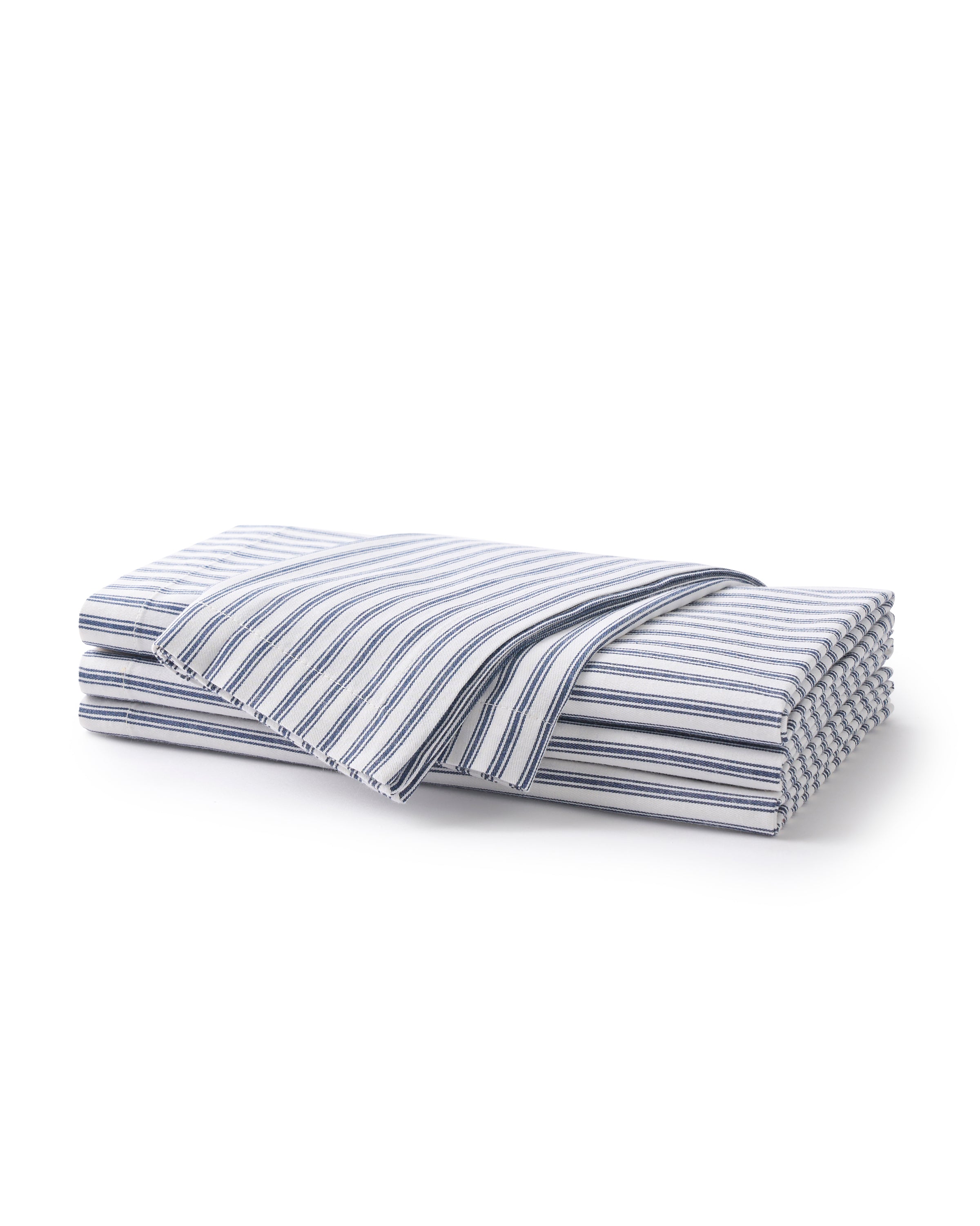 A neatly folded stack of Petite Plumes Signature Twill Napkin in Navy French Ticking is shown, with one partially unfolded on top. The vertical navy and white stripes add a classic, clean look to these cotton textiles, perfect for a festive tablescape.