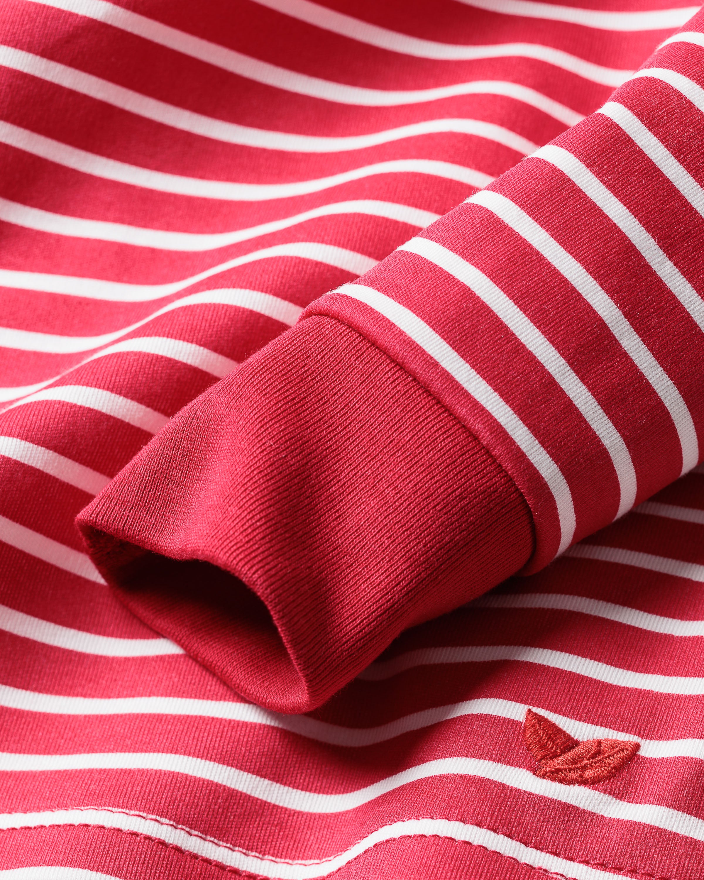 The Kids Pima Snug Fit Pajama Set in Red Stripe by Petite Plume features a close-up of red and white striped fabric with a folded cuff, perfect for sleepwear. The Pima Cotton material is textured and includes a small red embroidered leaf near the bottom.