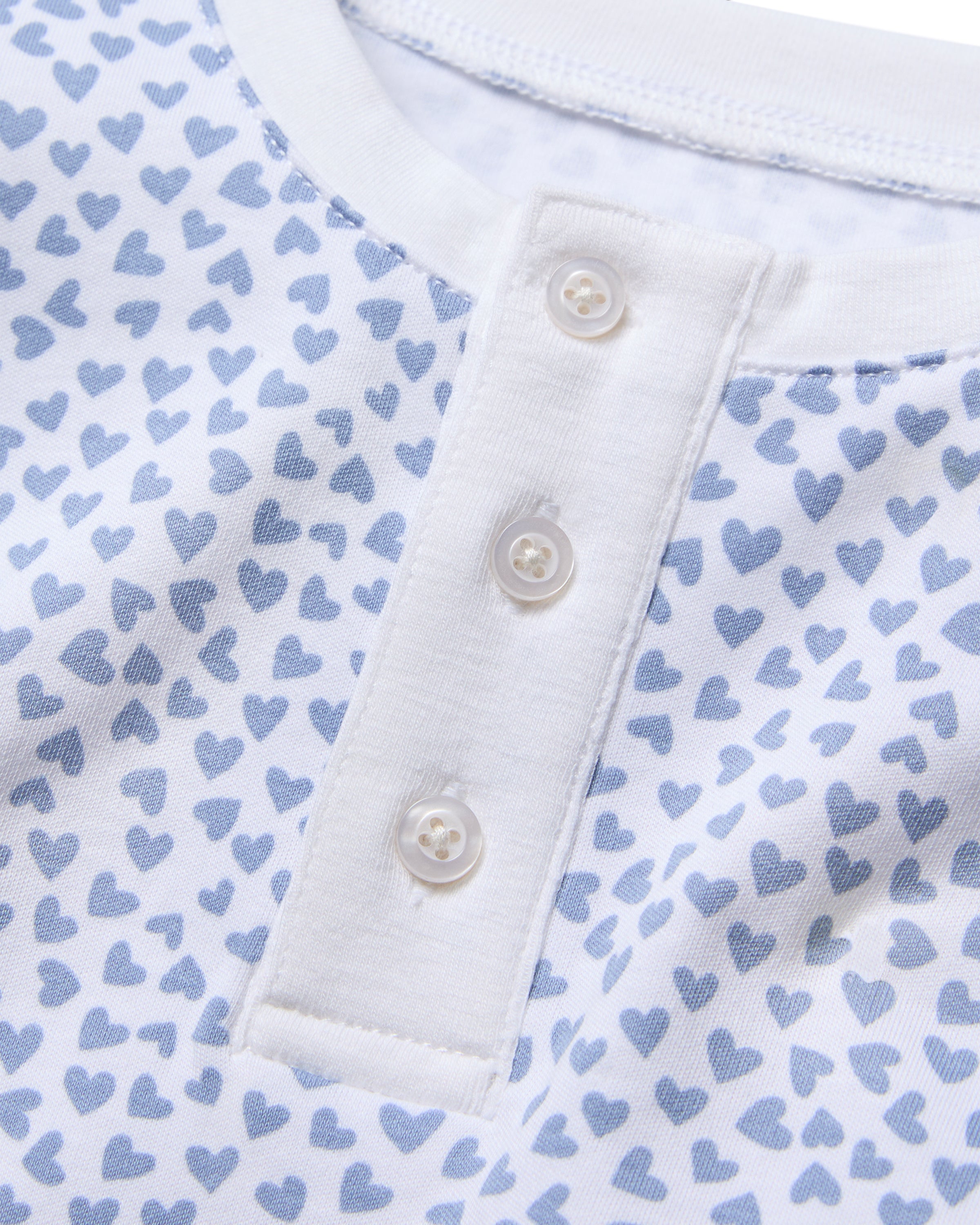 A close-up of the Kids Pima Snug Fit Pajama Set in Bluehearts by Petite Plume features a soft Pima Cotton white shirt with light blue heart patterns and a henley neckline with three white buttons, embodying coordinated style.