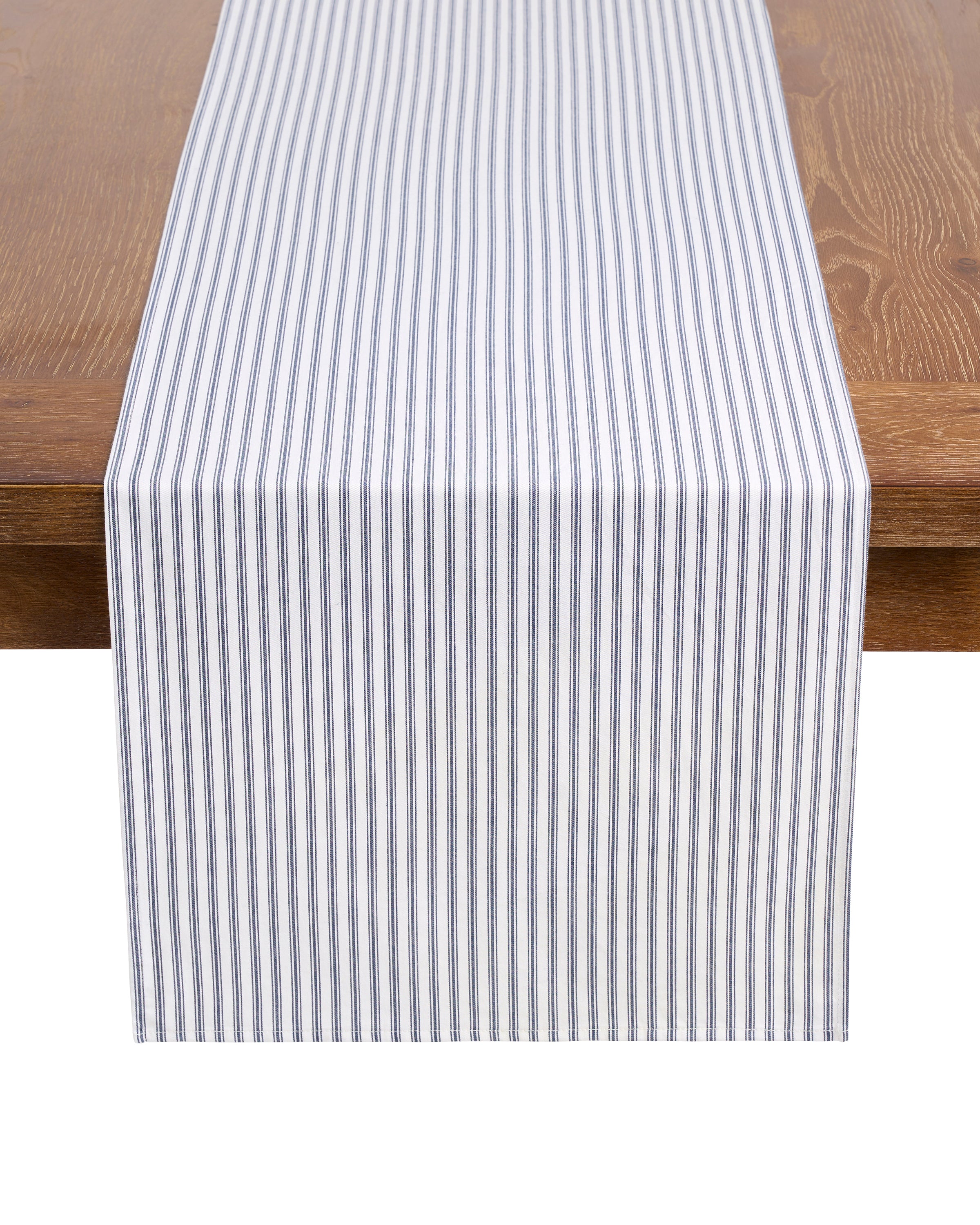 A wooden table features a festive tablescape with a cotton table runner in navy and white vertical stripes, part of the Signature Twill Table Linen set in Timeless Toile & Navy French Ticking by Petite Plume.