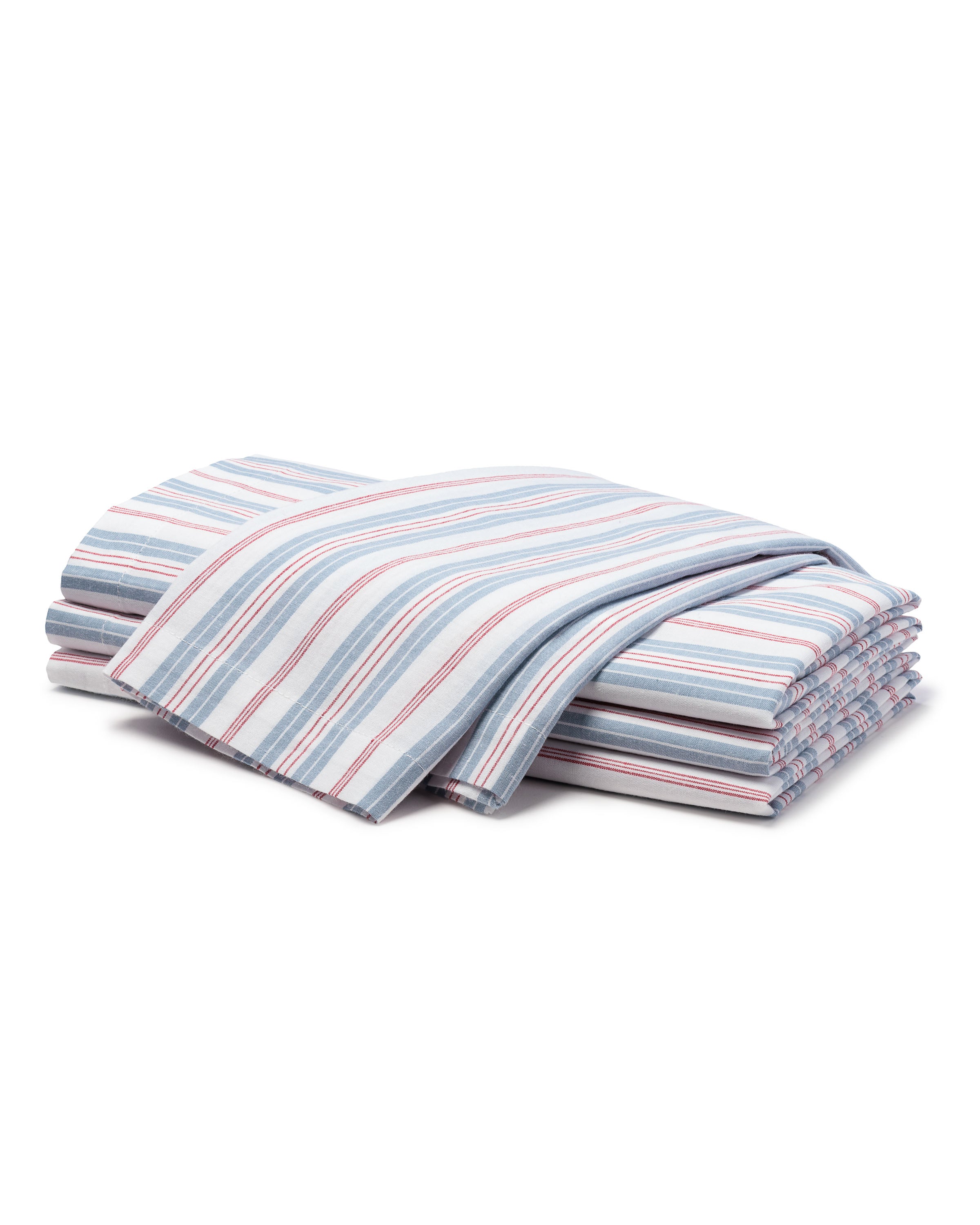 A neatly folded Signature Twill Table Linen Set in Vintage French Stripe by Petite Plume, featuring pastel stripes of blue, red, and white, sits beside other Petite Plume prints. These stacked linens create a clean and organized appearance.