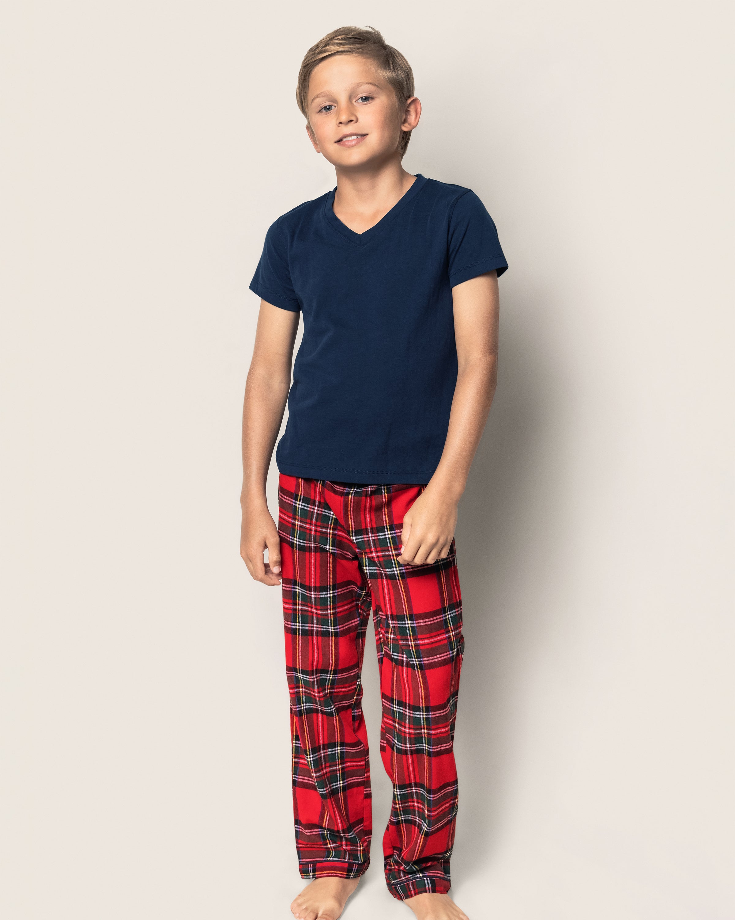 A boy stands against a plain background, sporting a navy blue t-shirt and Petite Plumes Kids Brushed Cotton Pajama Pants in Imperial Tartan, with a relaxed pose and slight smile.