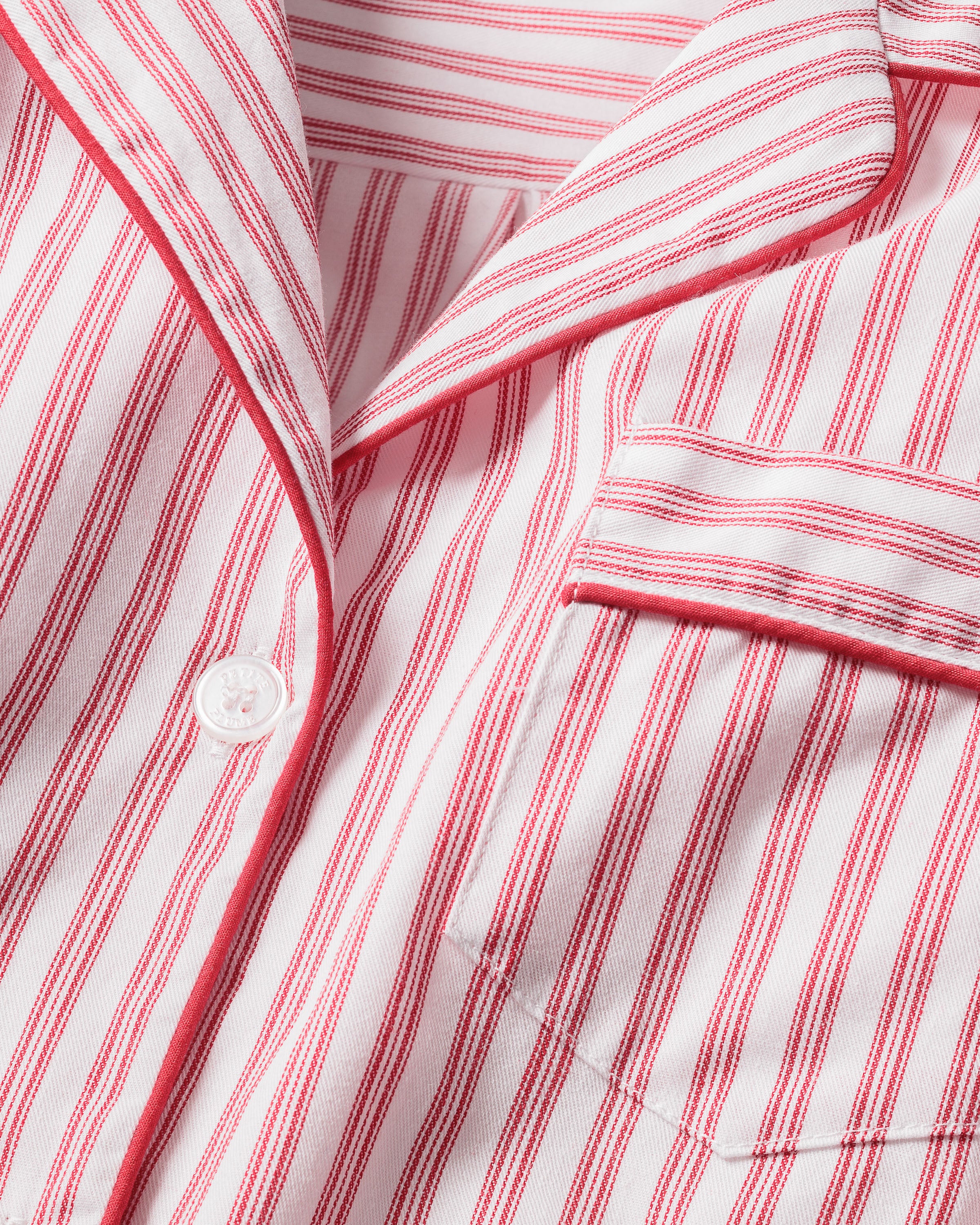 The Kids Twill Pajama Set in Antique Red Ticking by Petite Plume features a white fabric shirt with red vertical stripes, crafted from yarn-dyed cotton, a single white button, and a neatly sewn pocket on the left side. The collar is lined with red stripes for elegant style.