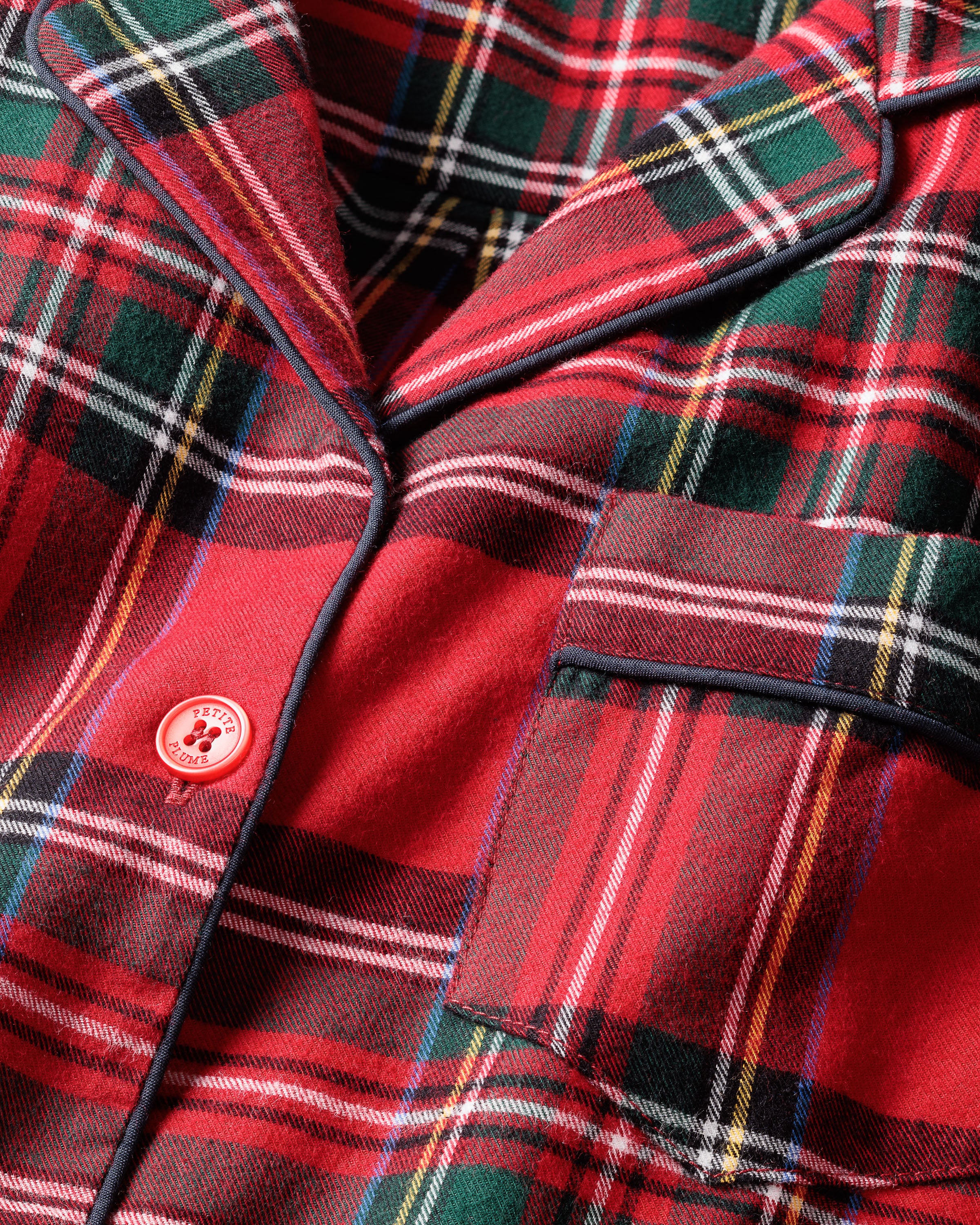 Close-up of Petite Plumes Kids Brushed Cotton Pajama Set in Imperial Tartan, showcasing a red plaid design with black, green, and white stripes. Made from soft, yarn-dyed cotton, it features a right-side pocket and a red button with a paw print—perfect for colder weather.